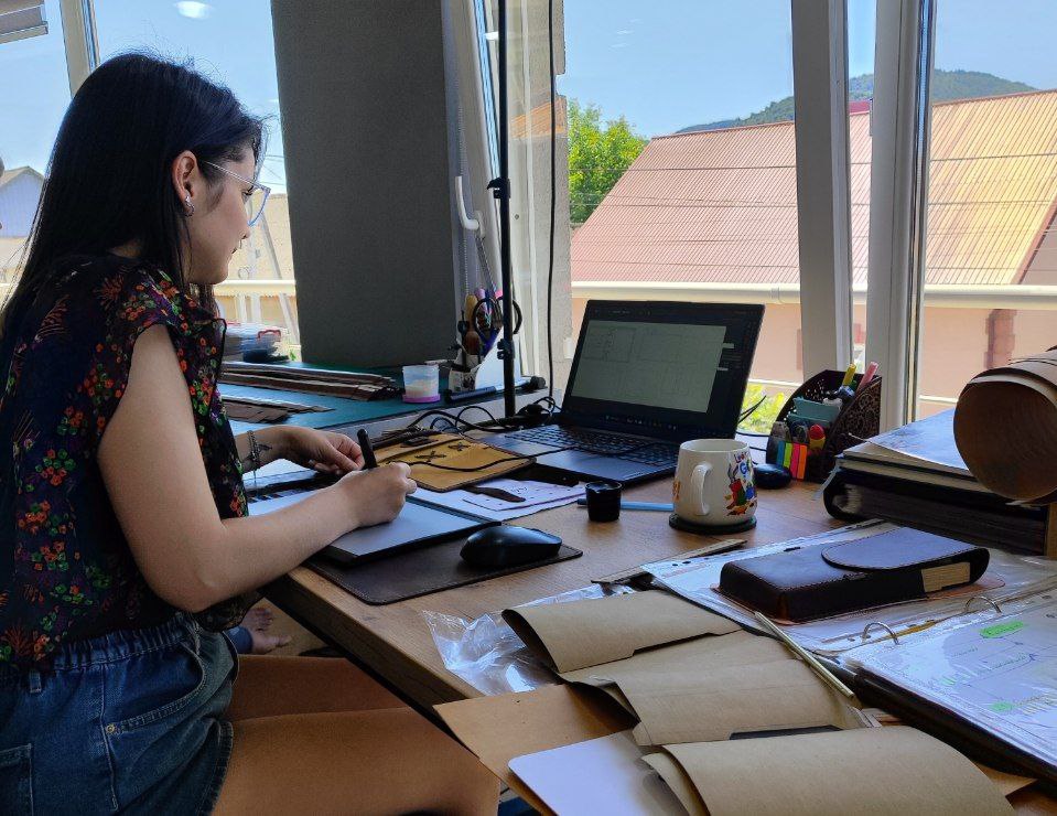 Vira, Mureli’s artist, designing new leather goods at her workshop desk with tools, sketches, and materials.