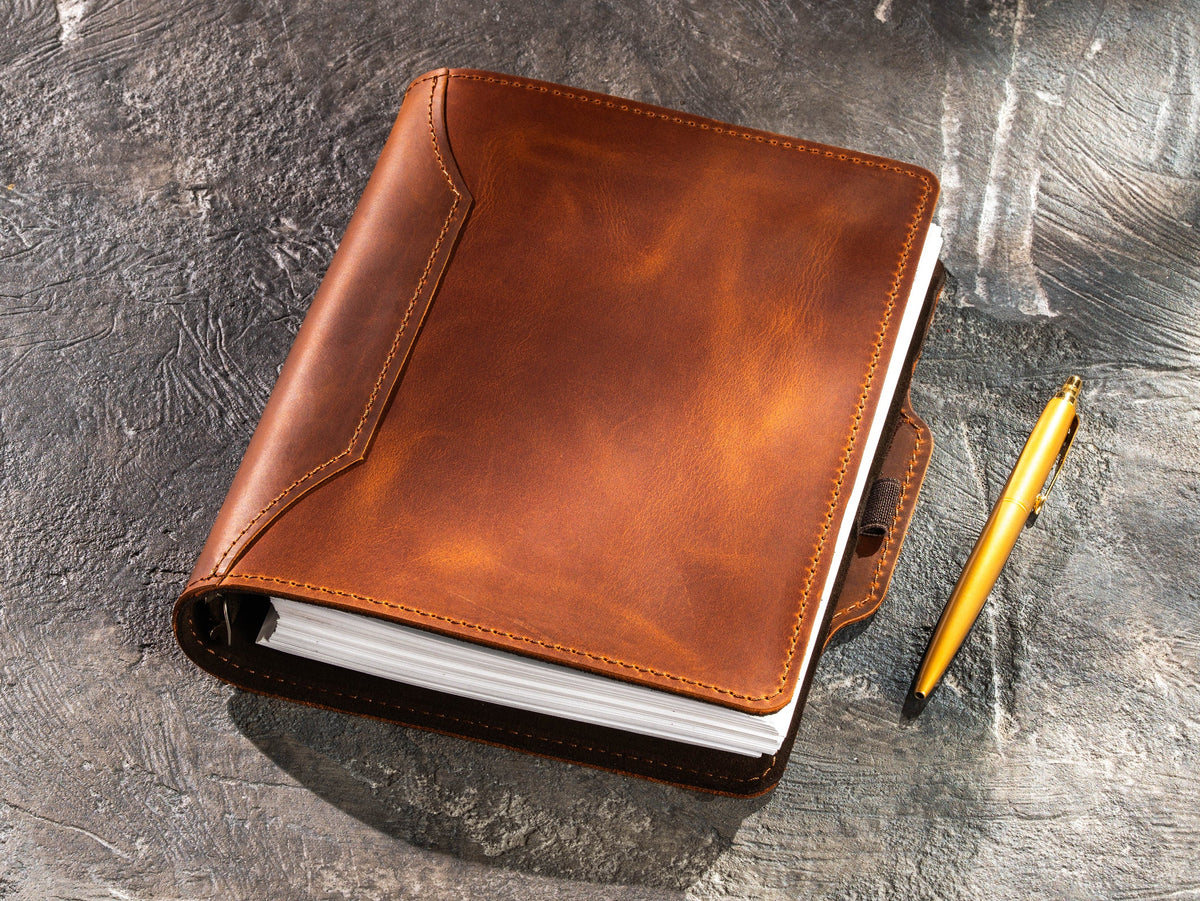 Copper Crazy Horse leather business notebook with decorative stitched front cover and gold pen beside the integrated holder