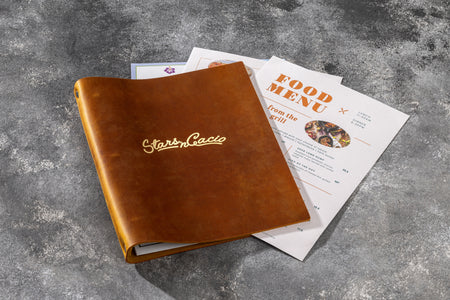 Flat-lay of an open leather menu binder with colorful food menu inserts