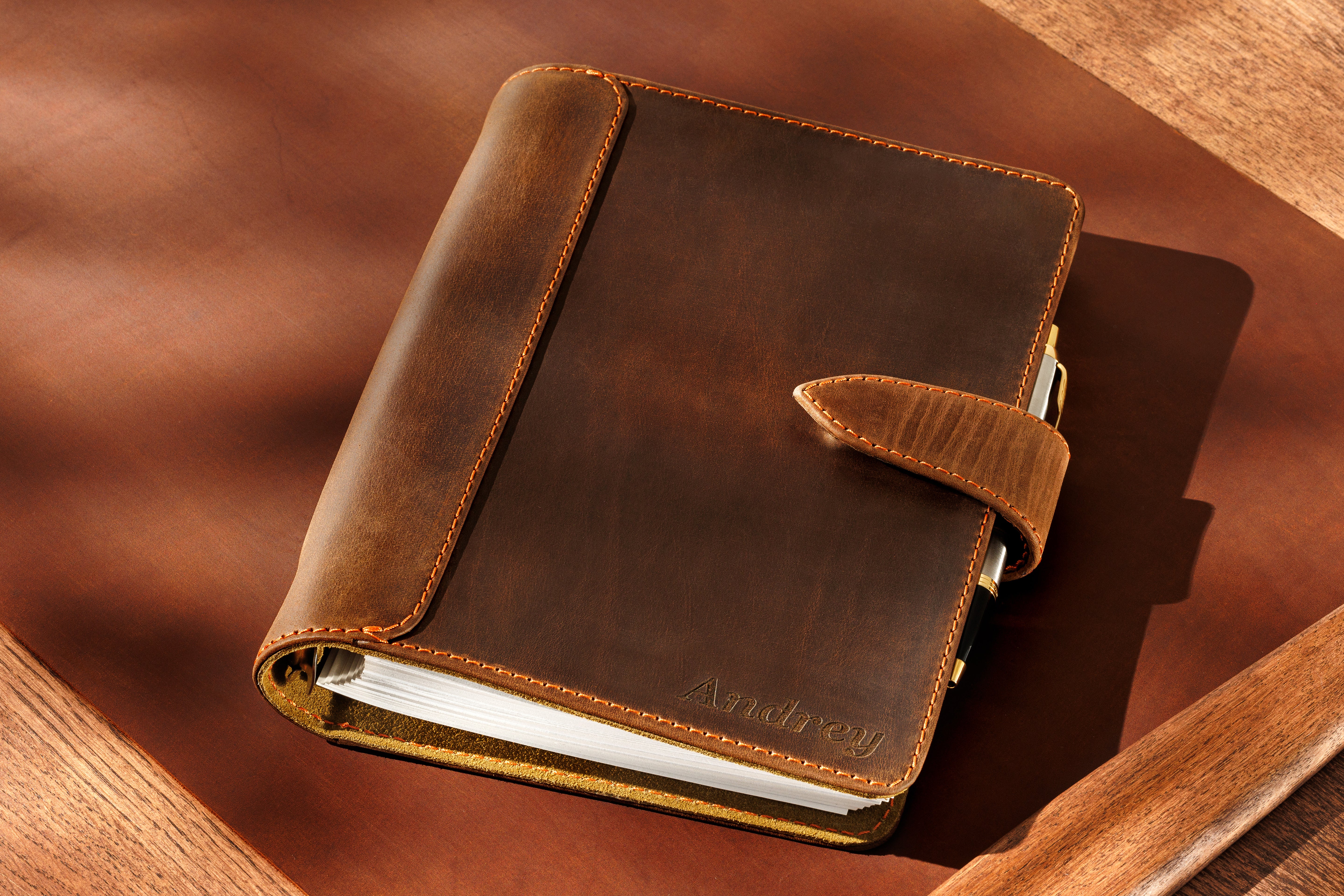 Premium dark brown leather notebook Mureli with pen and strap closure on wooden desk