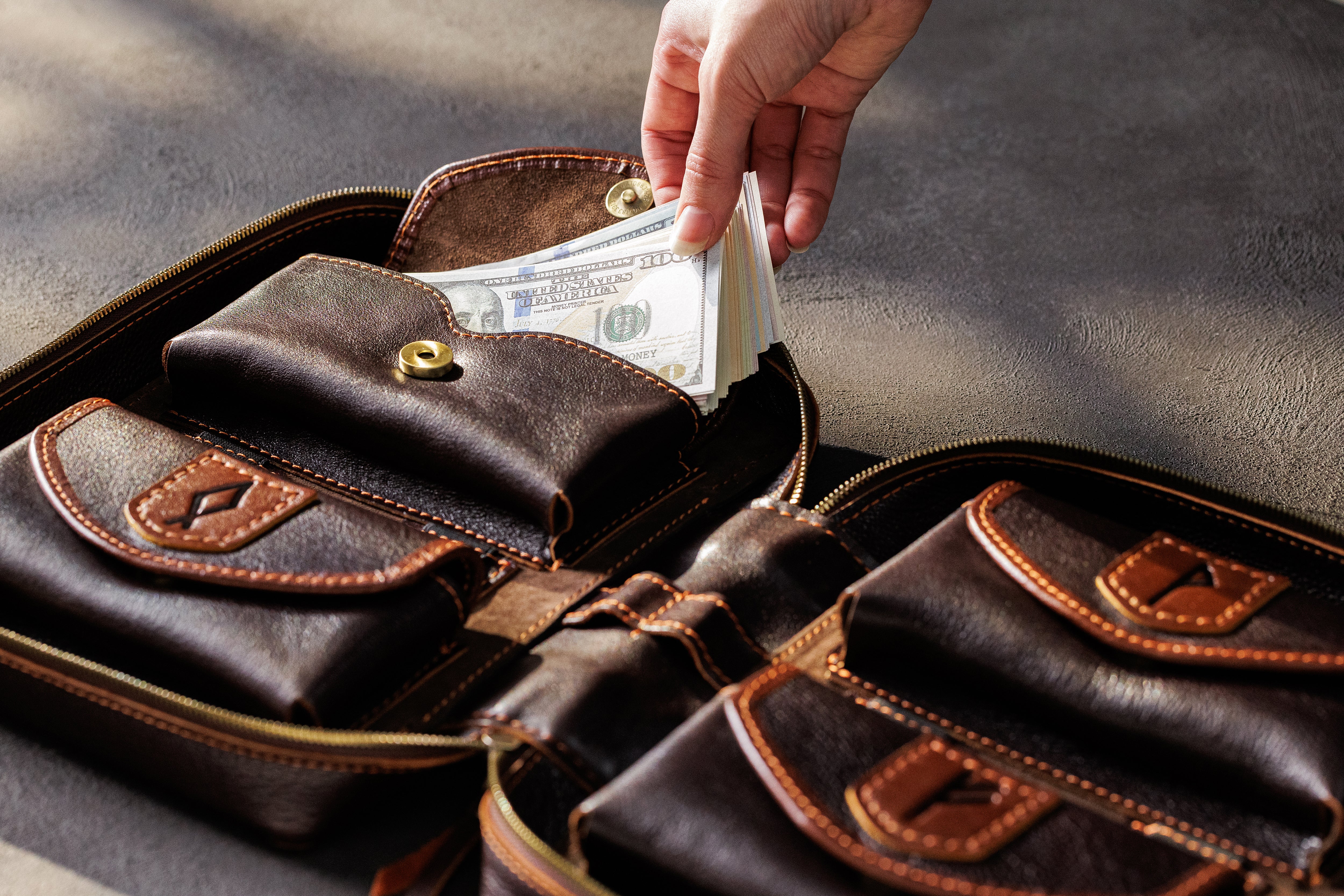 Hand placing US dollar bills into dark brown leather cash storage pocket for family budgeting