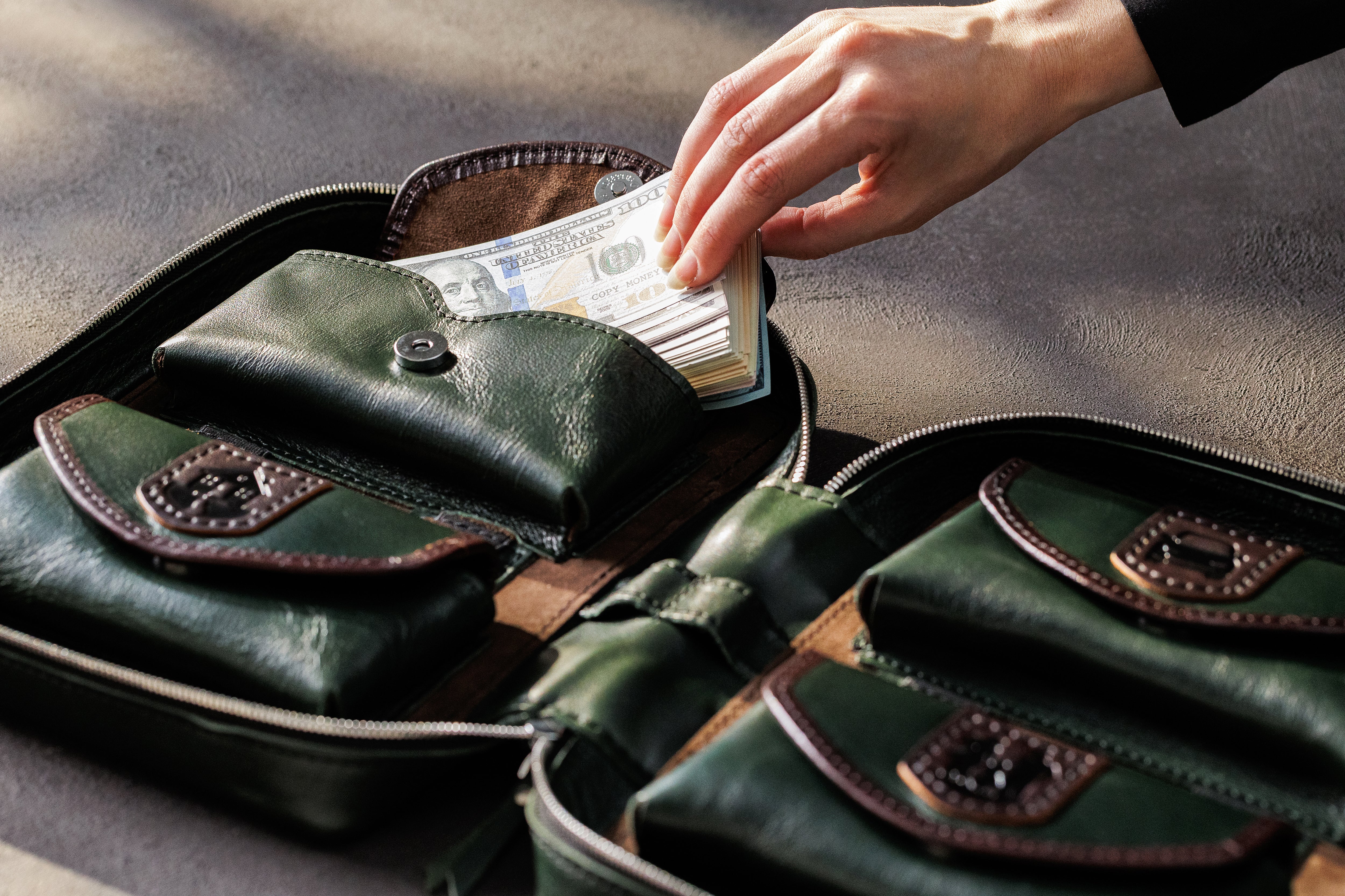 Hand removing US dollar bills from expandable dark green leather money storage pocket