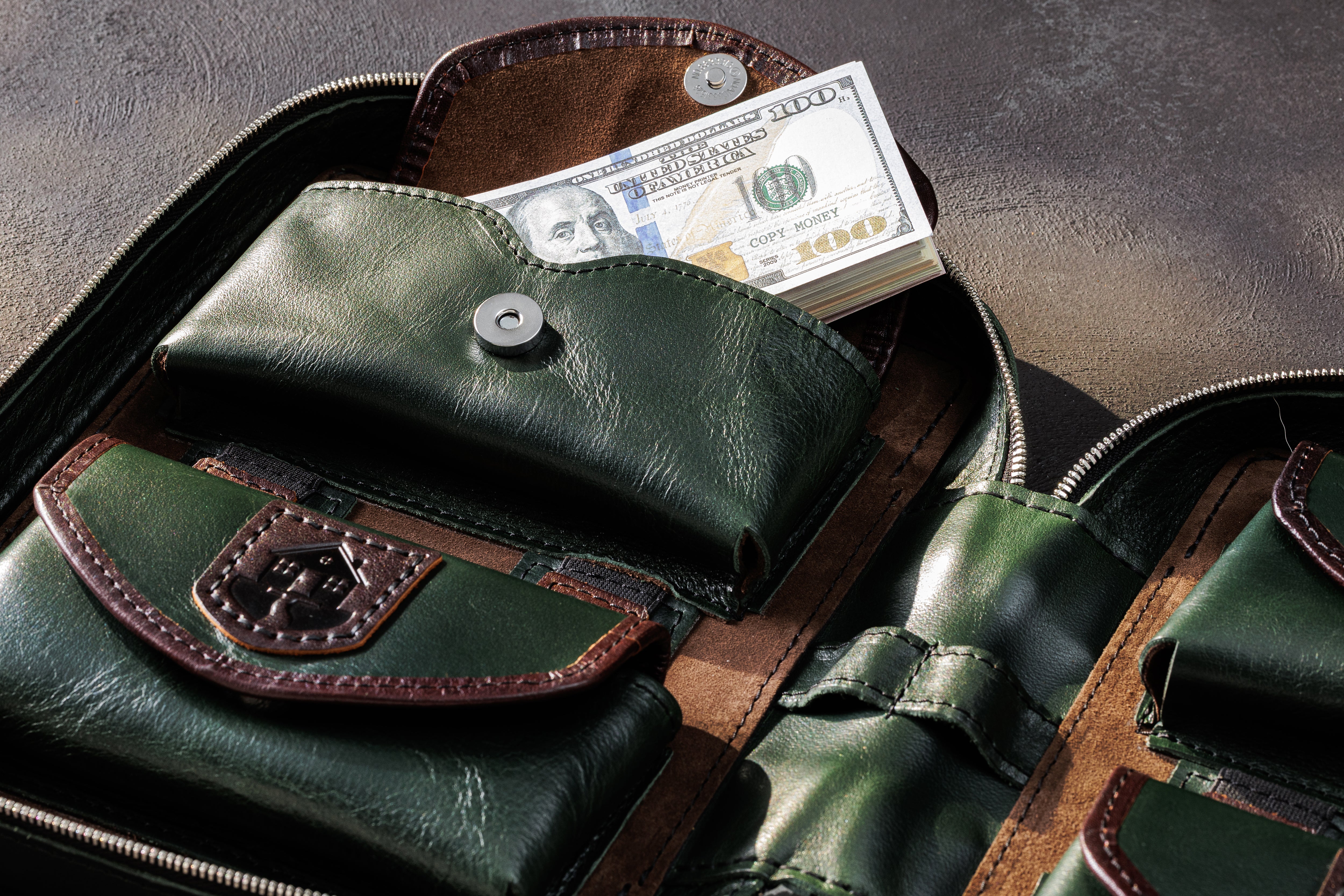 Dark green leather cash pocket holding US dollar bills inside a multi-currency money organizer
