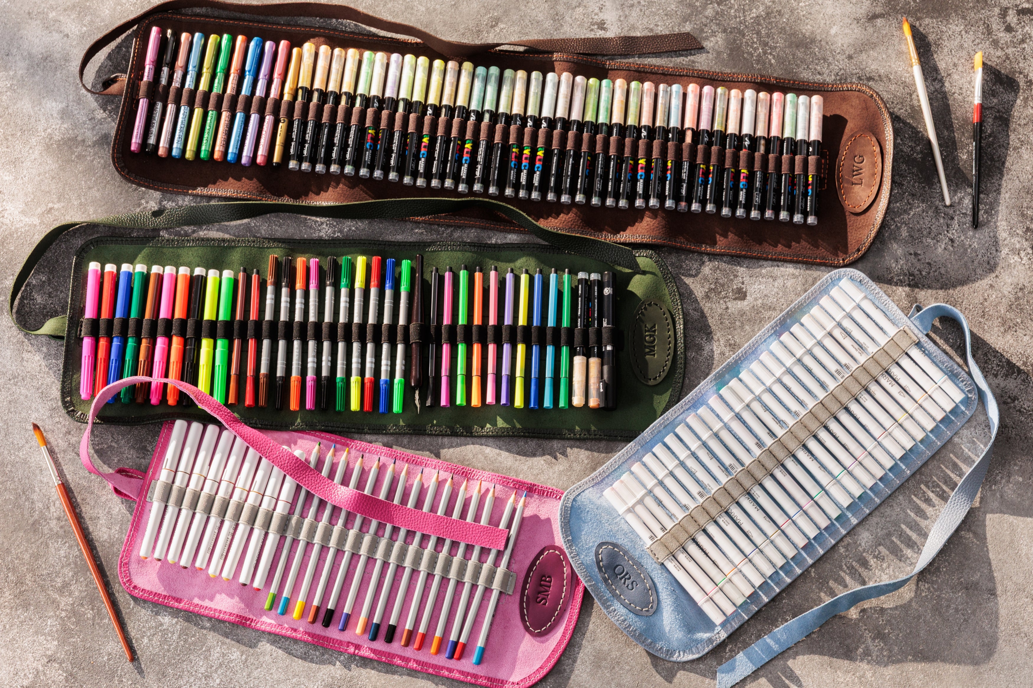 Collection of art supplies including colored pencils, markers, and pastels in various cases on a textured surface.