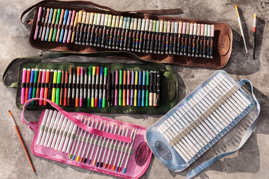 Collection of art supplies including colored pencils, markers, and pastels in various cases on a textured surface.