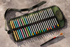 Set of colored pencils in a green case with a brush on a gray surface