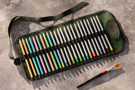 Set of colored pencils in a green case with a brush on a gray surface