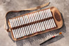 Set of colored pencils in a brown leather case on a gray surface with a paintbrush.