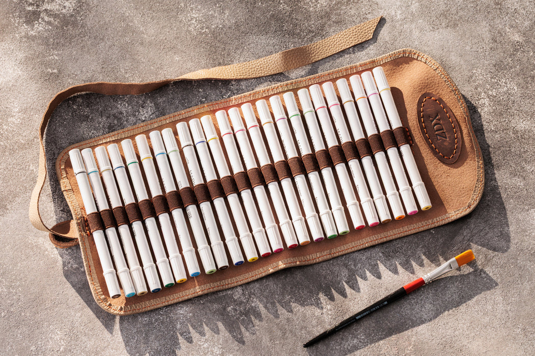 Set of colored pencils in a brown leather case on a gray surface with a paintbrush.