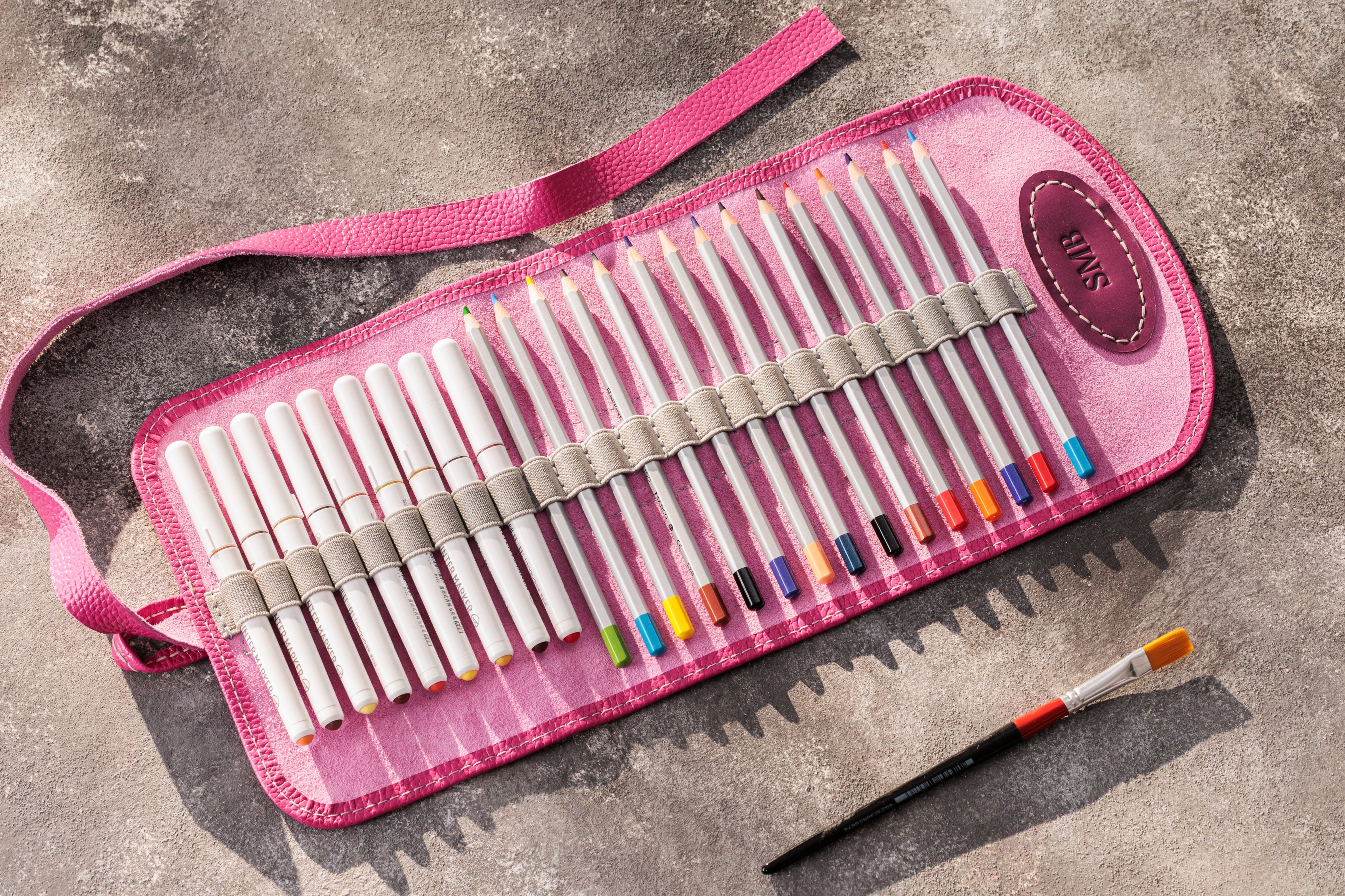 Pink case with colored pencils and a paintbrush on a gray surface