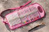 Pink case with colored pencils and a paintbrush on a gray surface