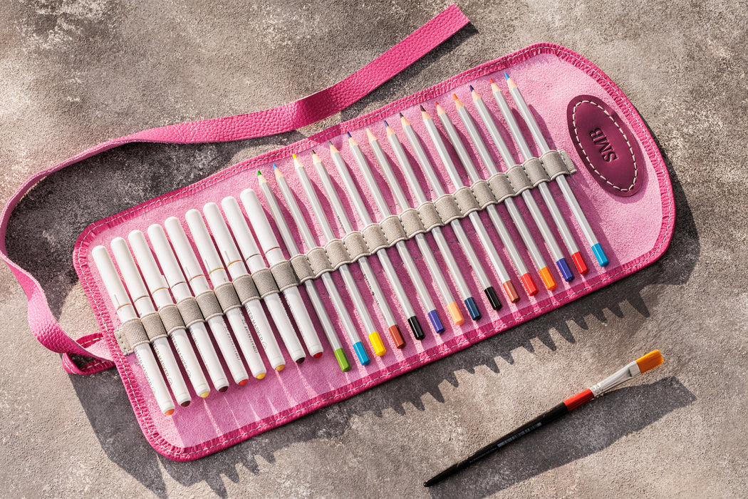 Pink case with colored pencils and a paintbrush on a gray surface