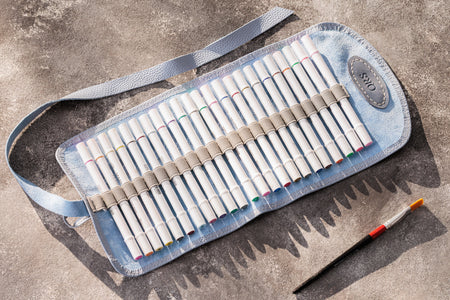 Set of colored pencils in a blue roll-up case on a concrete surface