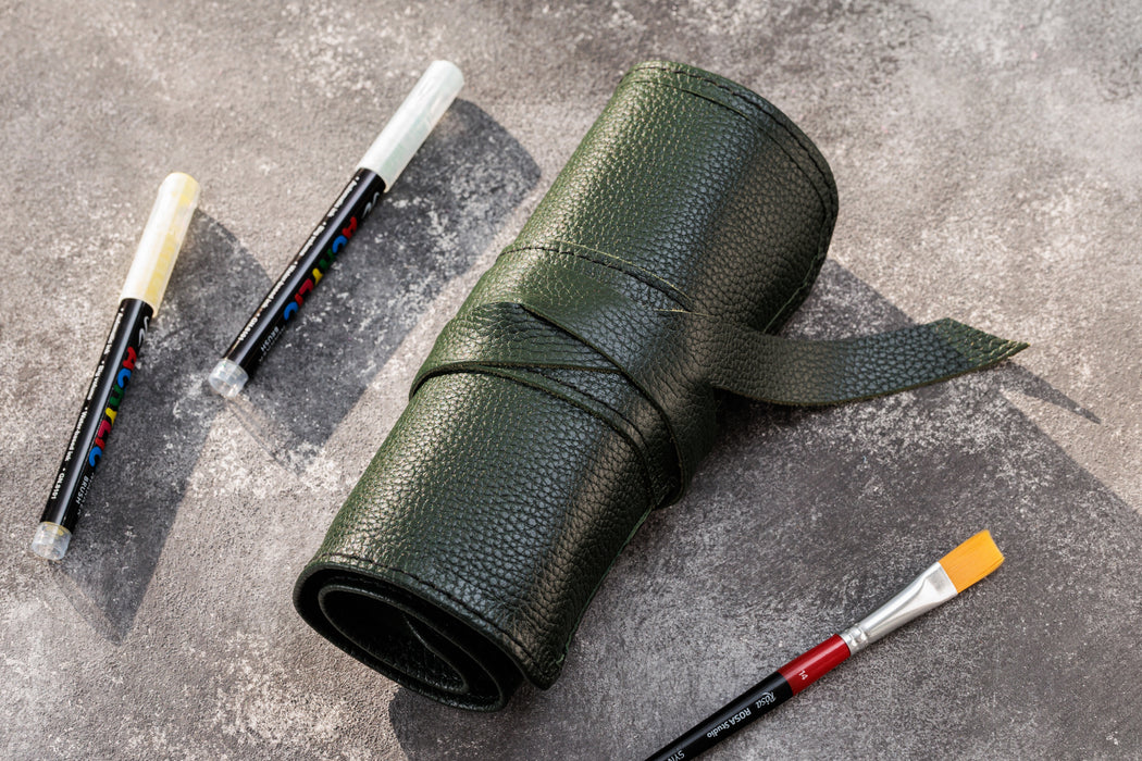Green leather pencil case with markers and paintbrushes on a gray surface