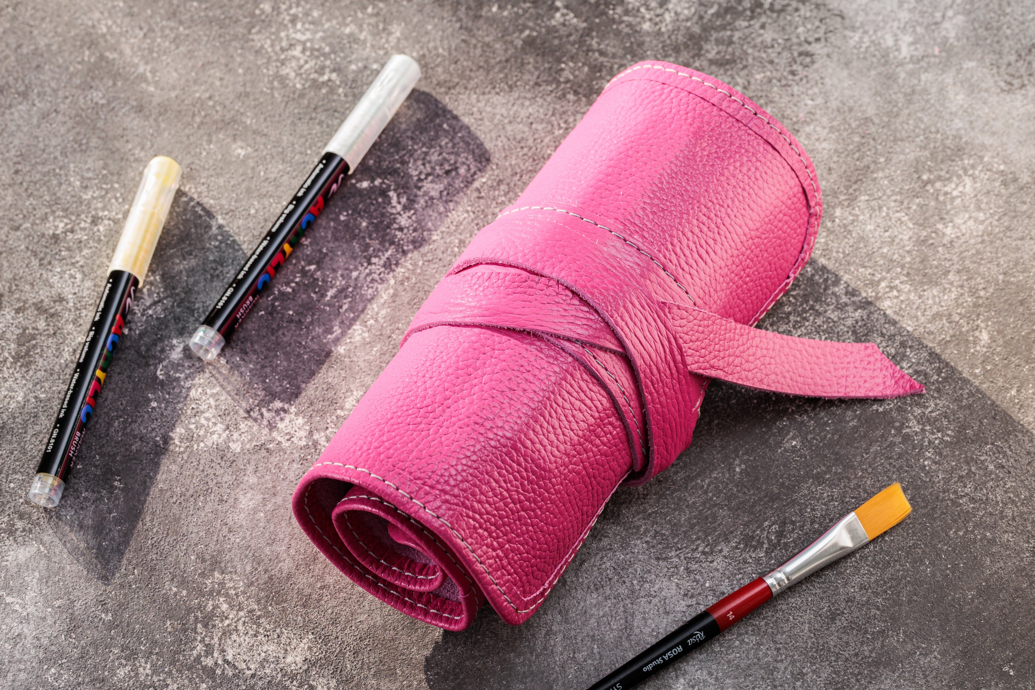 Pink leather roll with paintbrushes on a textured surface