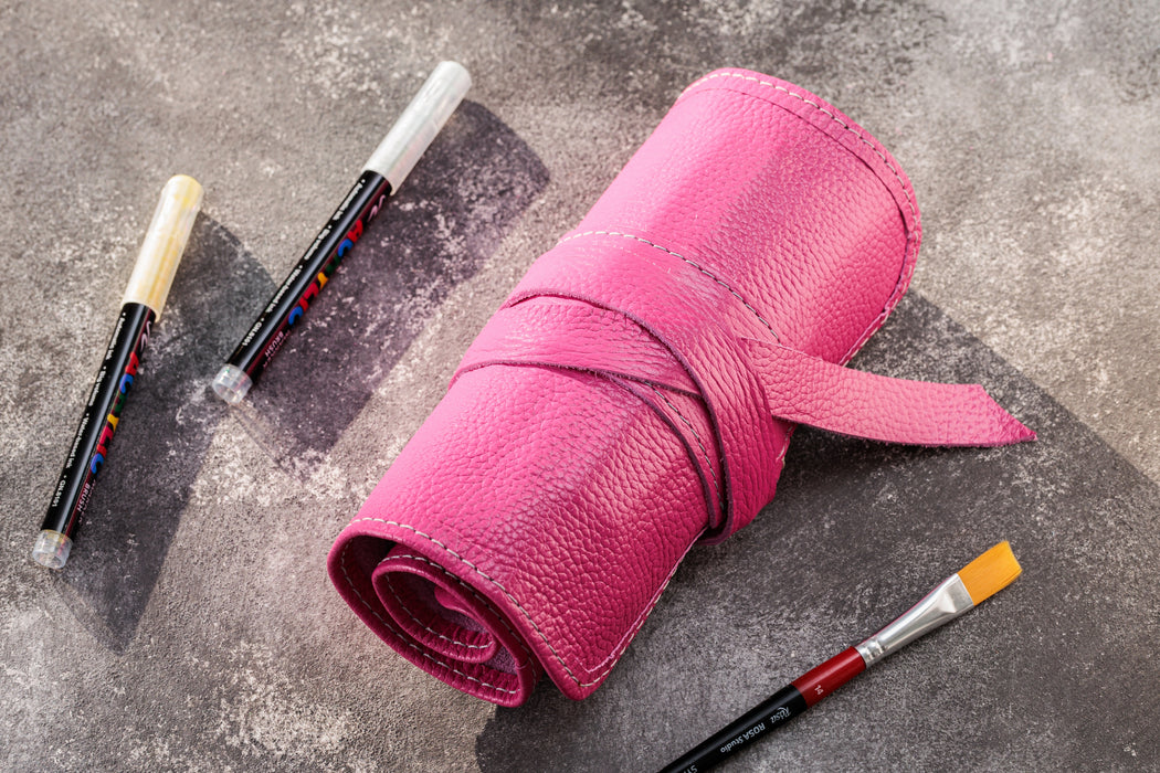 Pink leather roll with paintbrushes on a textured surface