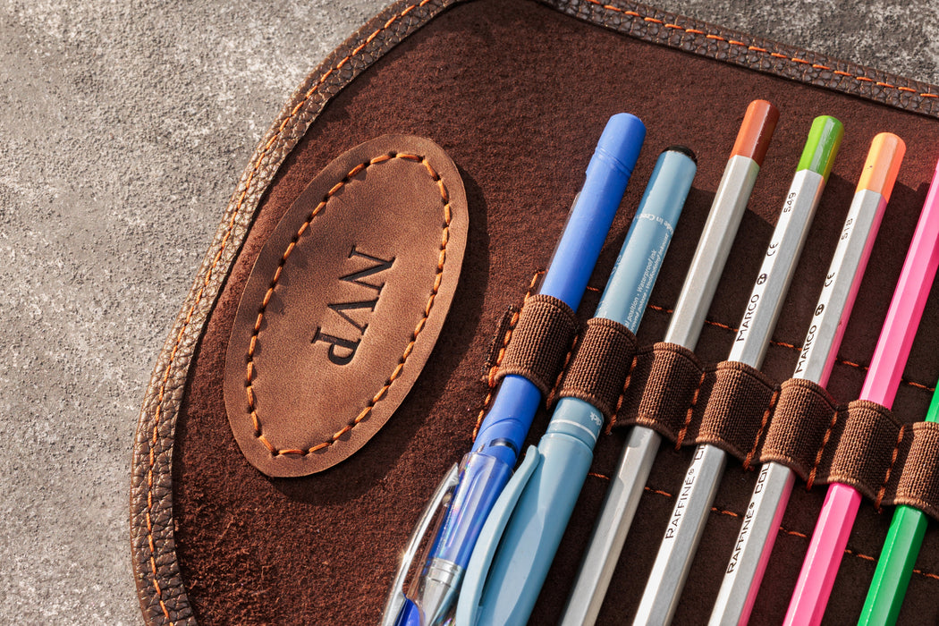 Set of colorful pens in a brown leather case with 'NVP' branding.