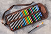 Set of colored pencils and a paintbrush in a brown leather case on a gray surface