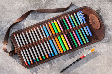 Set of colored pencils and a paintbrush in a brown leather case on a gray surface