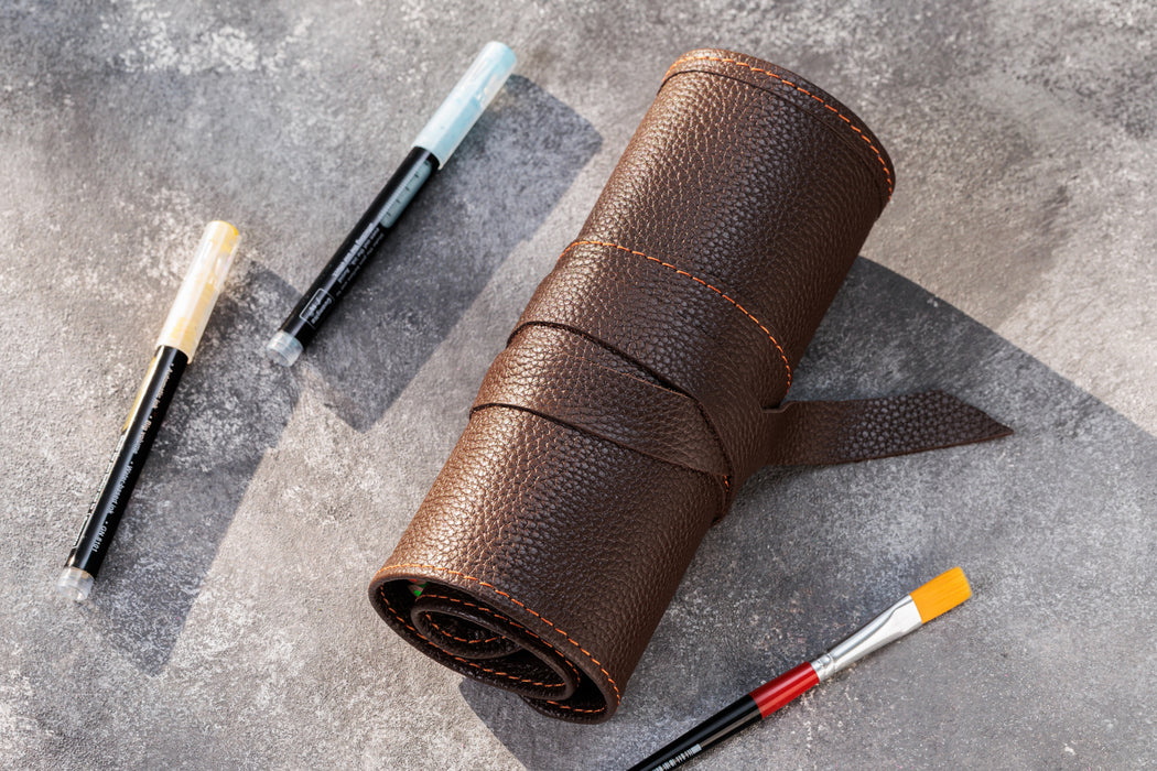 Brown leather roll with paintbrushes on a gray textured surface