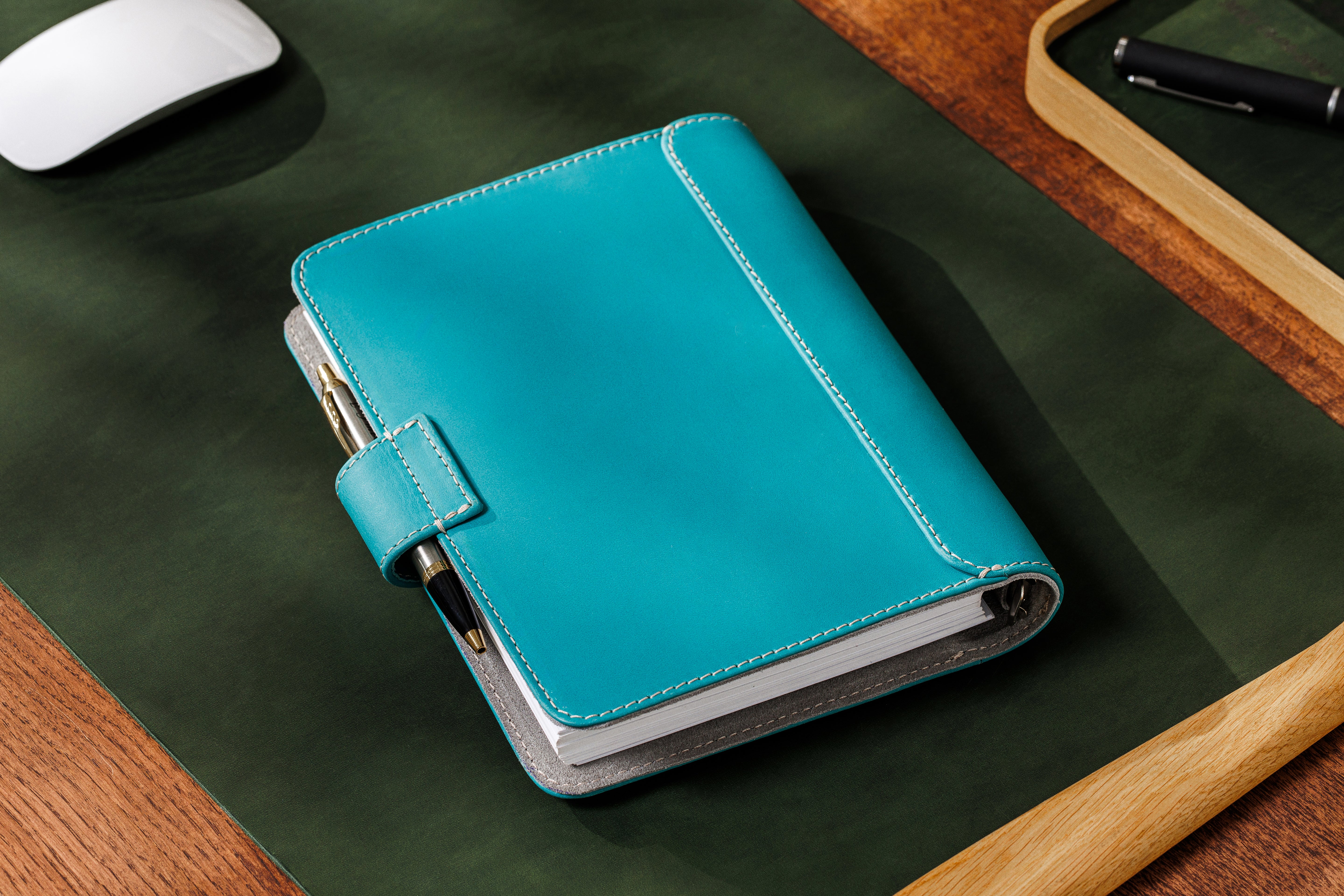 Mureli notebook in light blue leather next to laptop, pen, and coffee