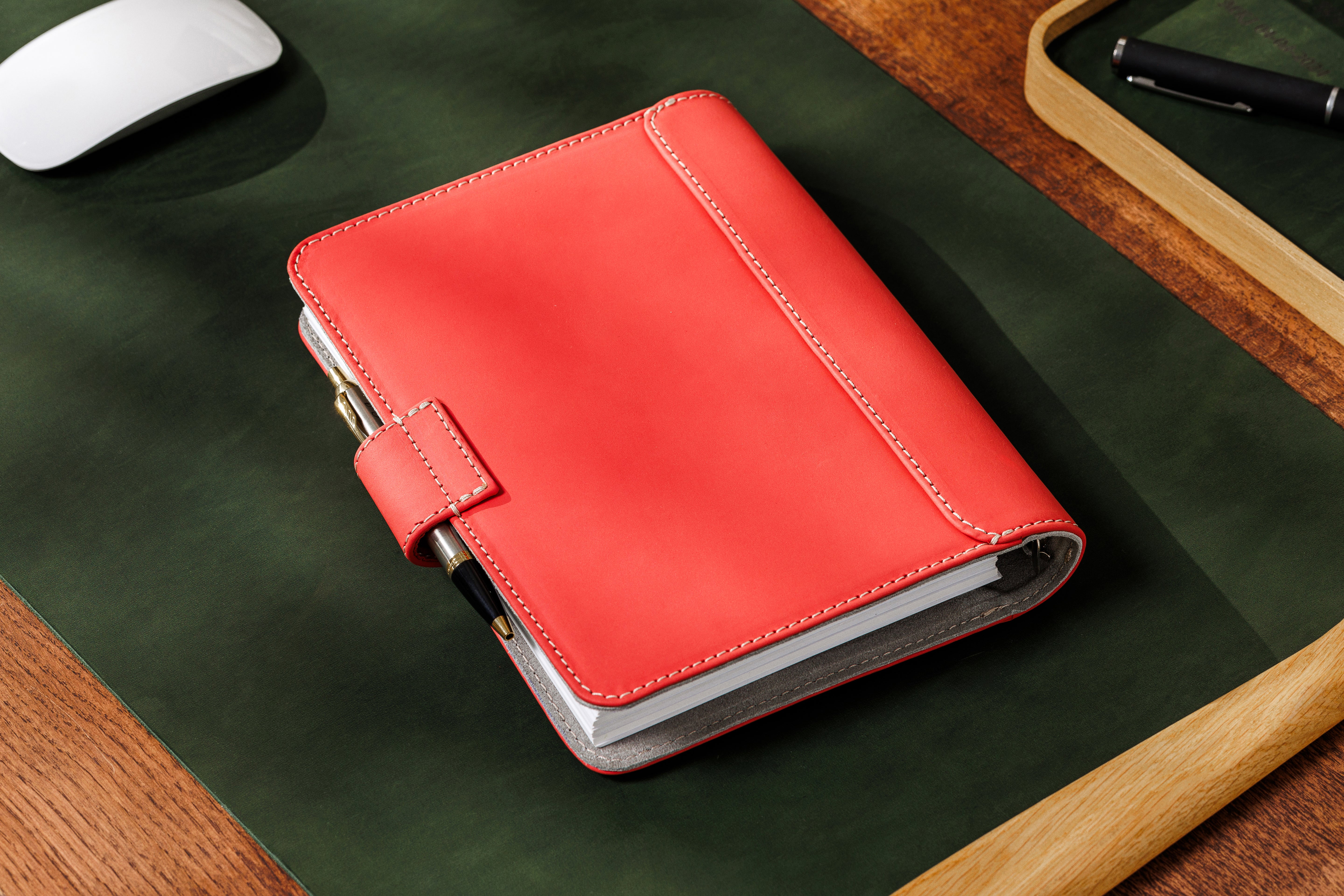 Bright coral leather notebook on wooden desk with premium workspace setup