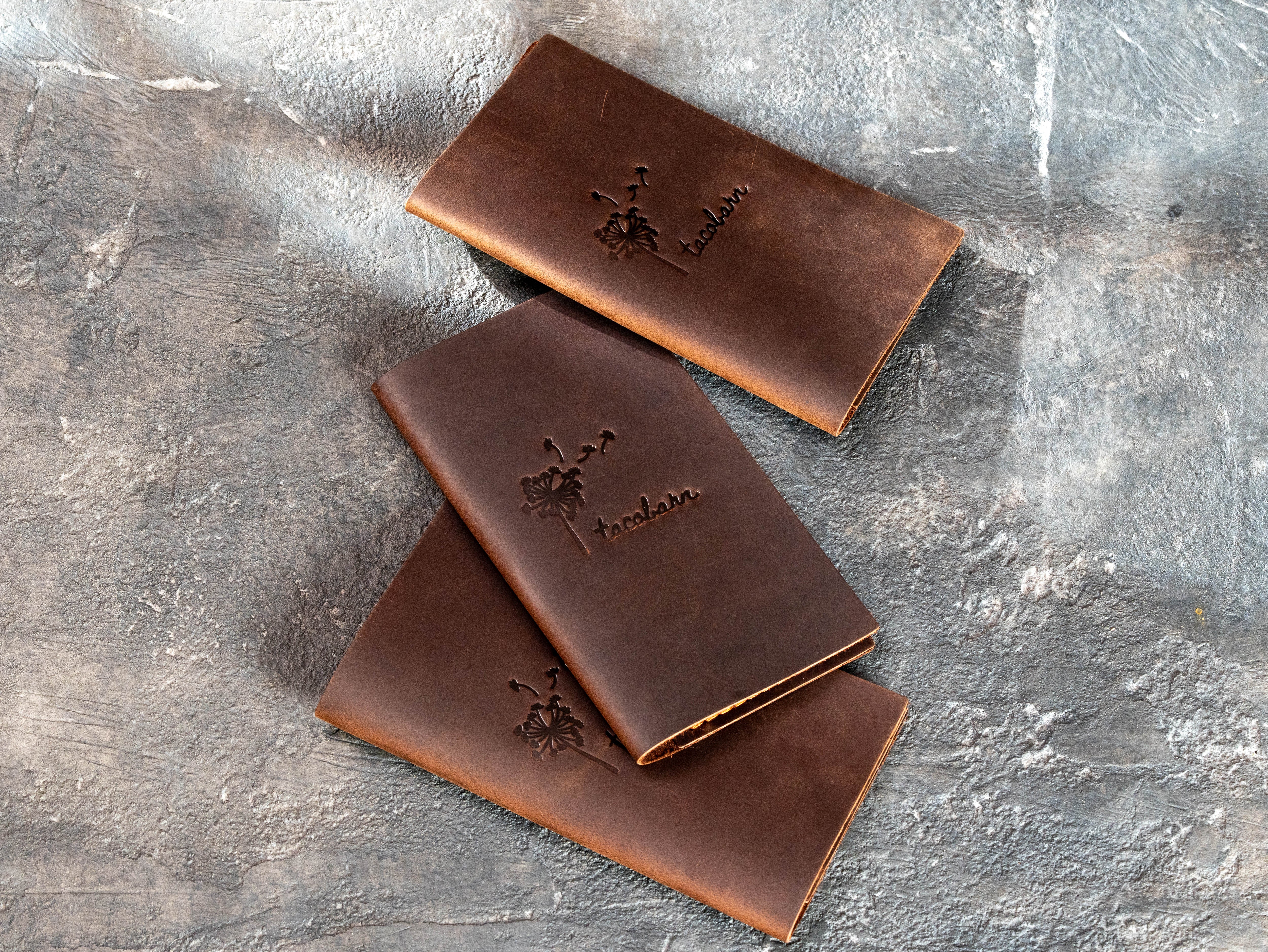 Three closed brown leather check presenters branded with Taco Bar dandelion artwork