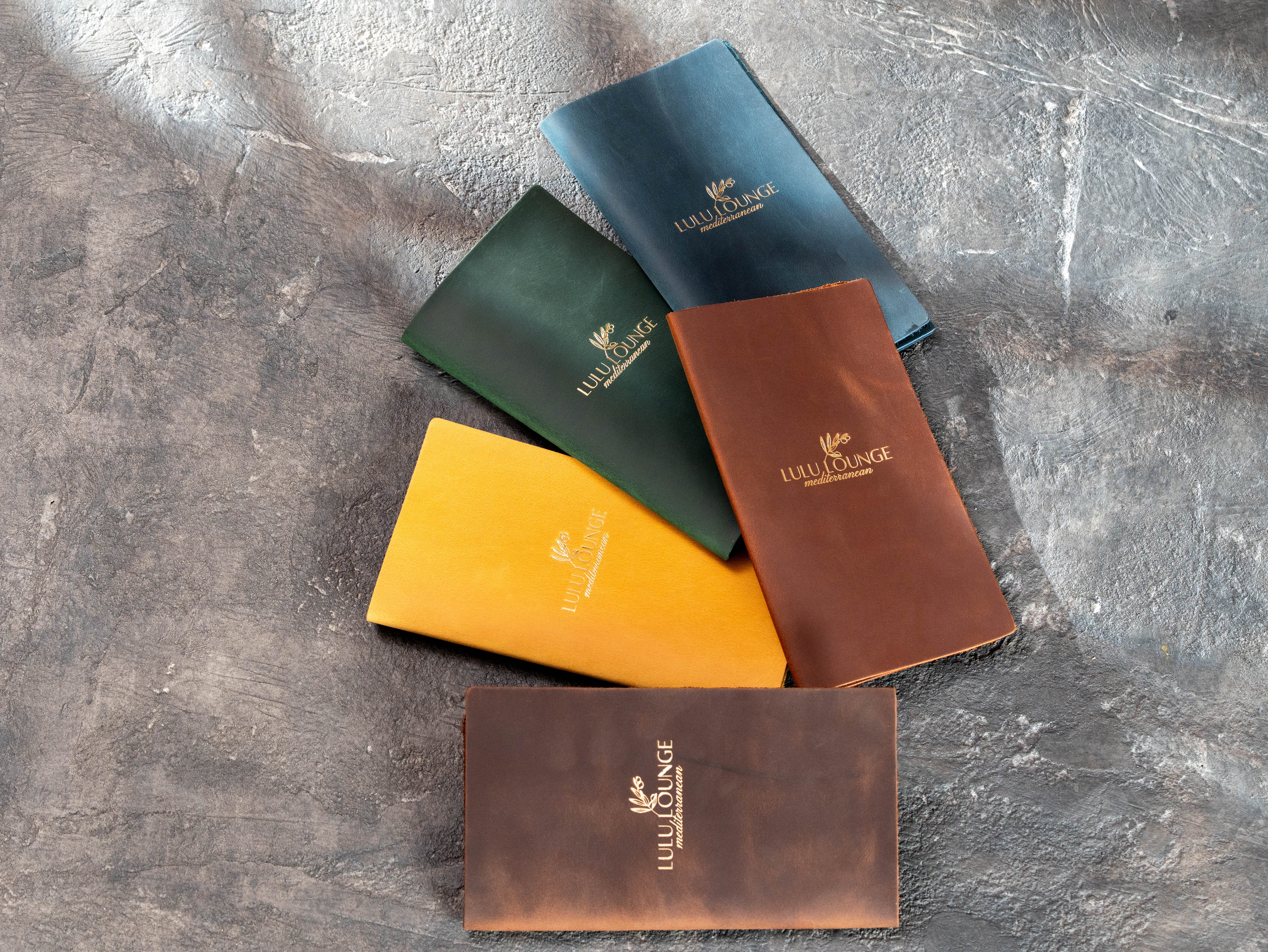 Multiple colored leather restaurant check presenter samples with custom business branding.