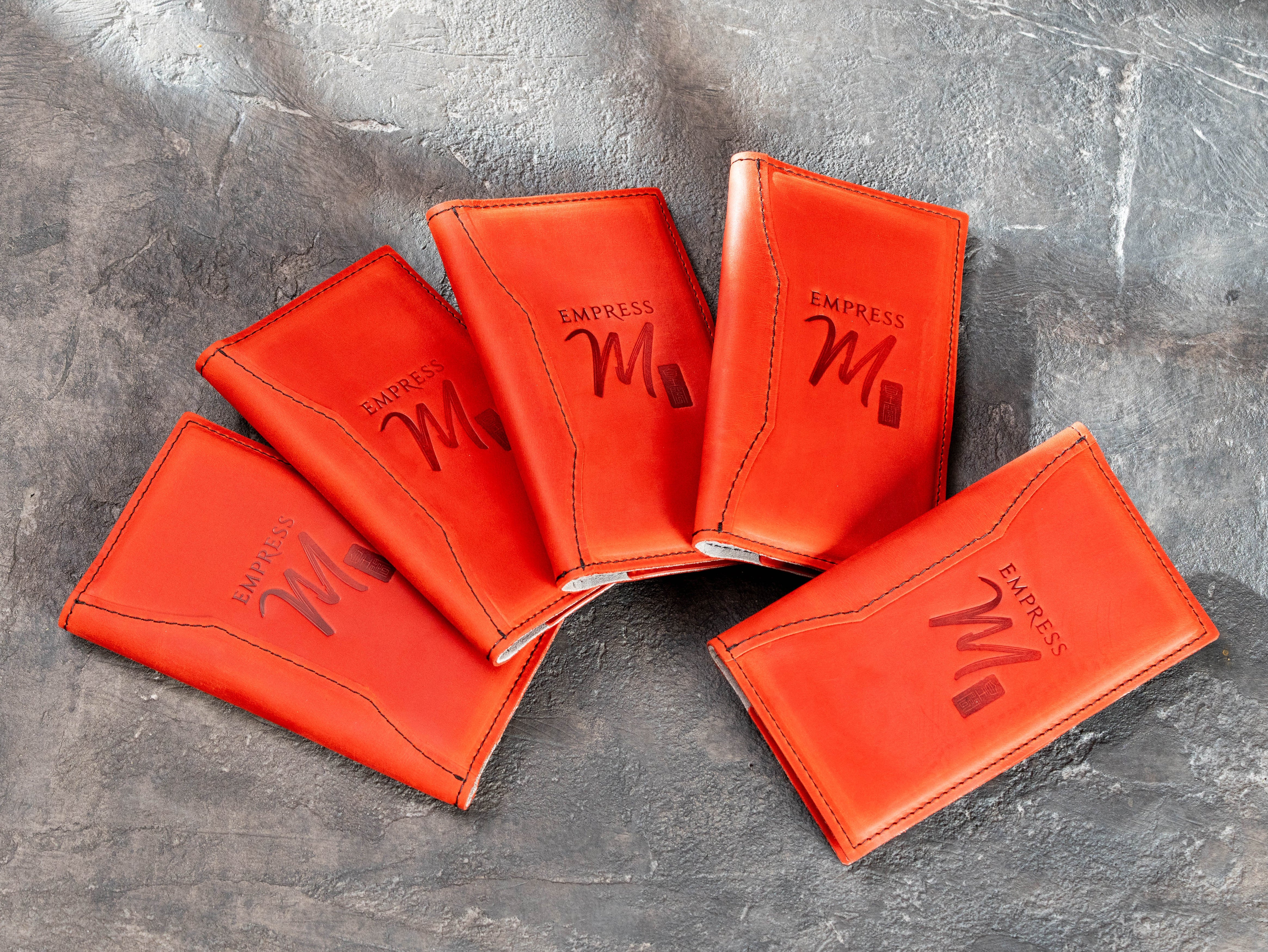 Red leather restaurant bill holders with stitched asymmetrical cover design and custom logo