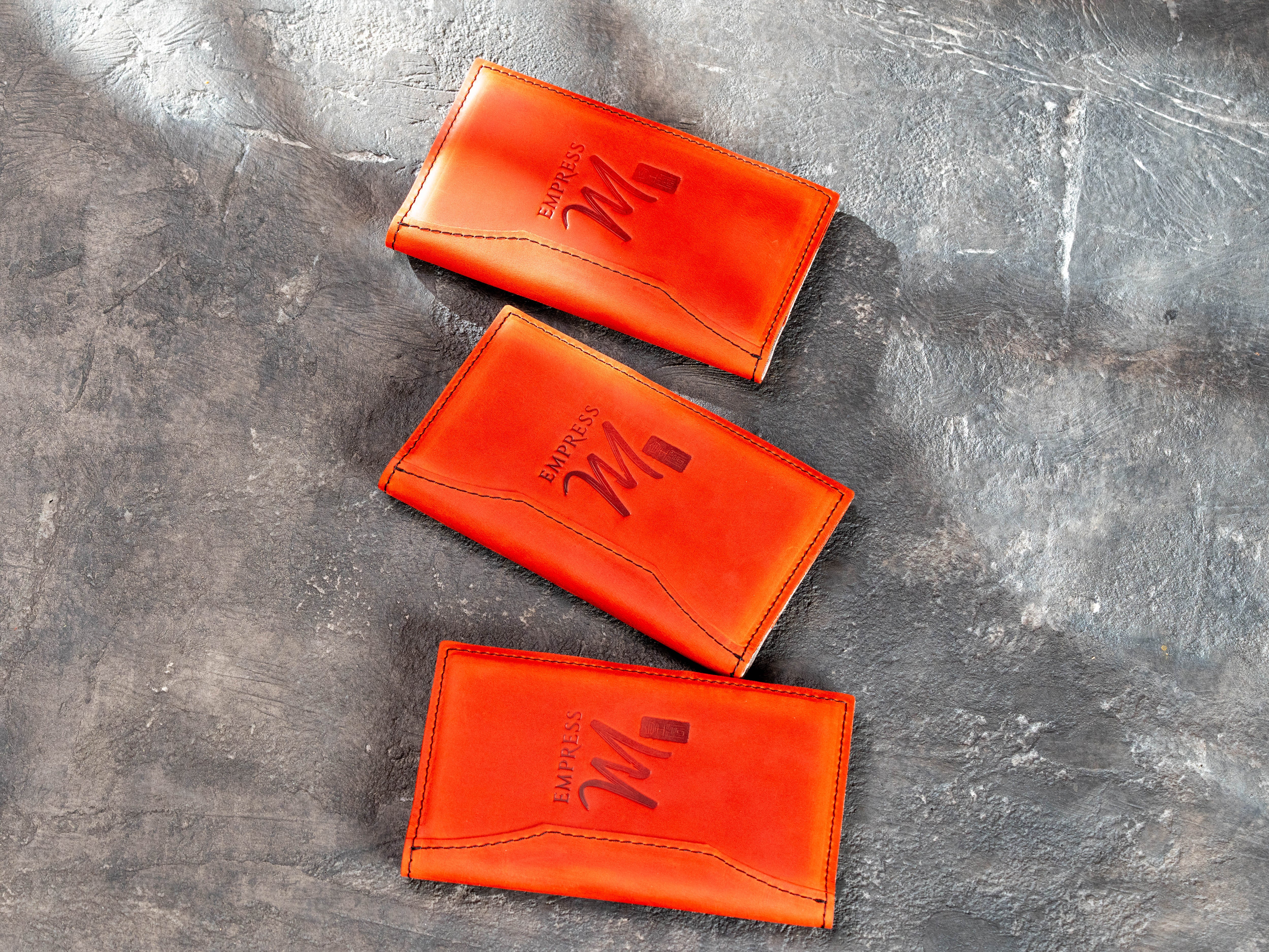 Red restaurant check presenters with custom embossed logo and decorative stitching