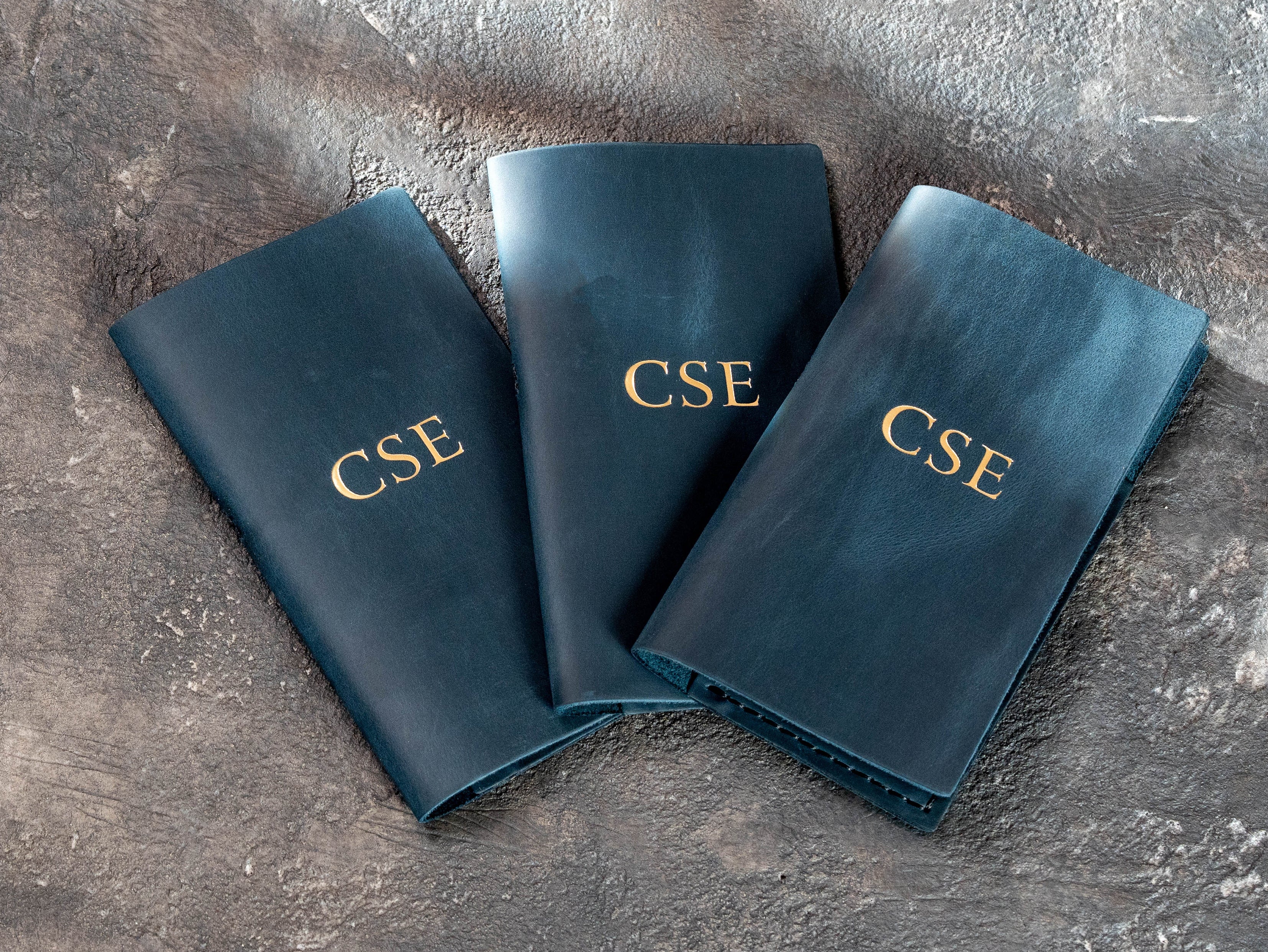 Three custom blue leather check presenters with gold initials for restaurant service