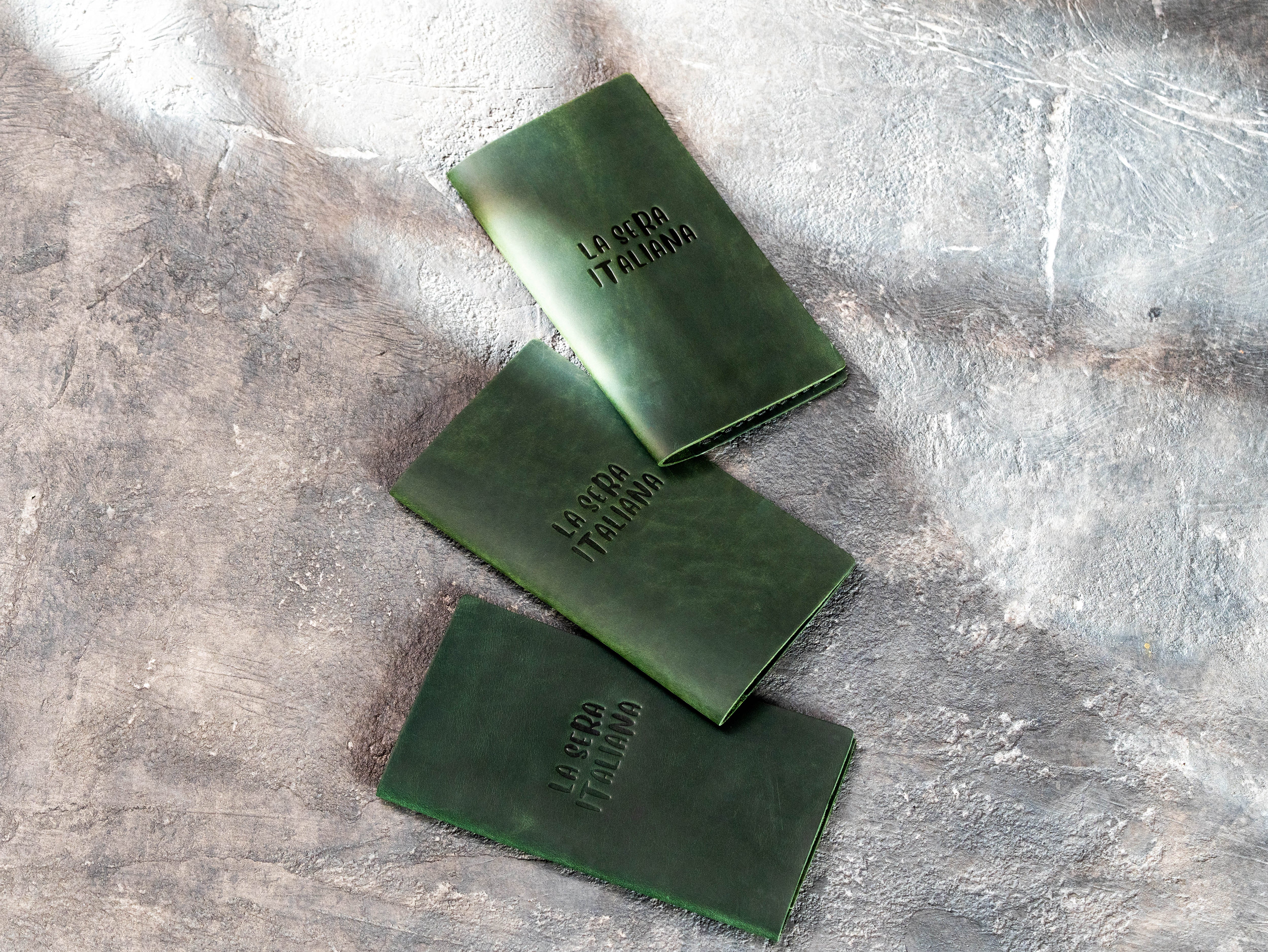 Dark green personalized restaurant bill holders with understated embossed branding