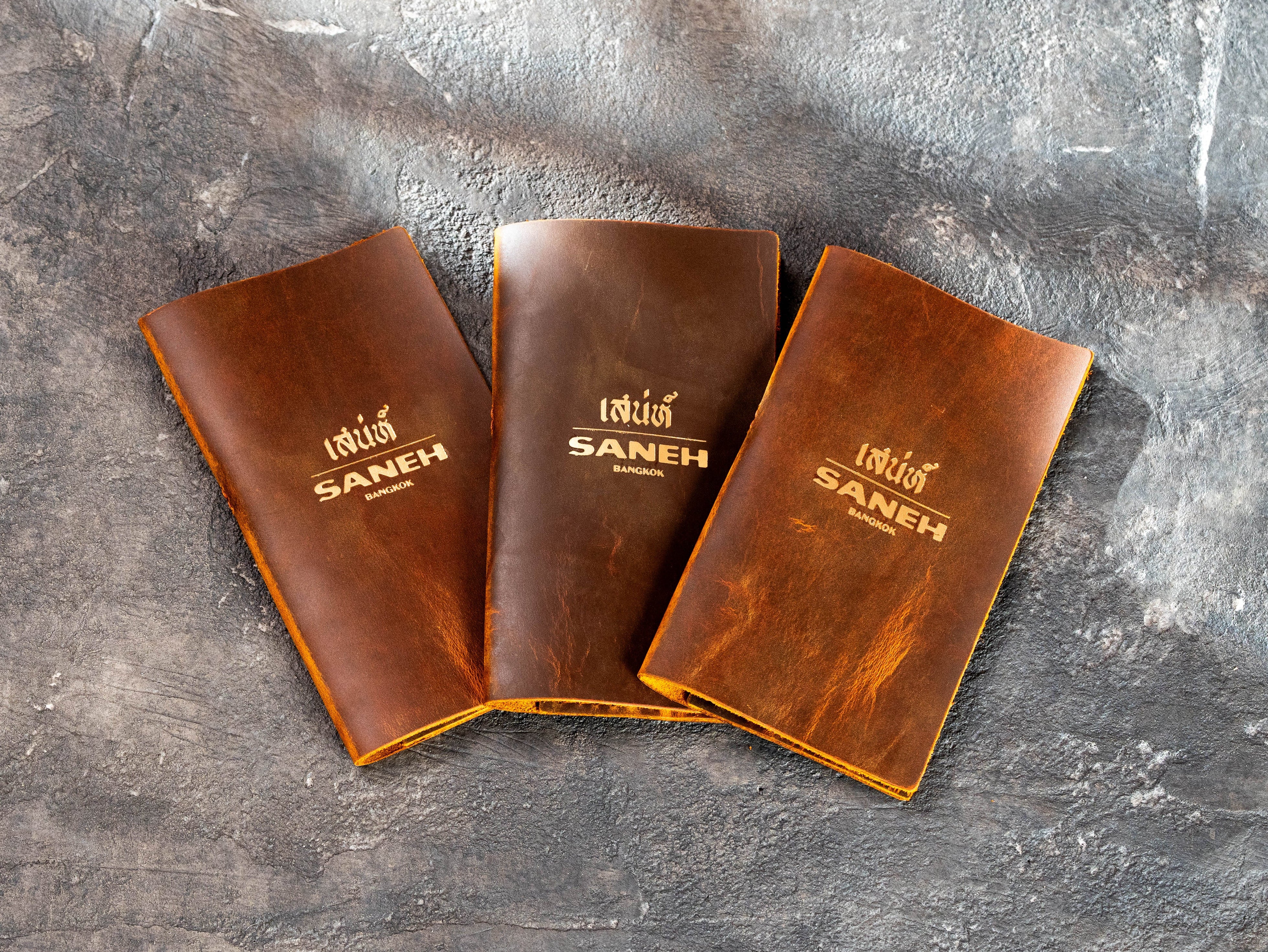 Chestnut leather restaurant check presenters with custom gold logo made by Mureli Workshop