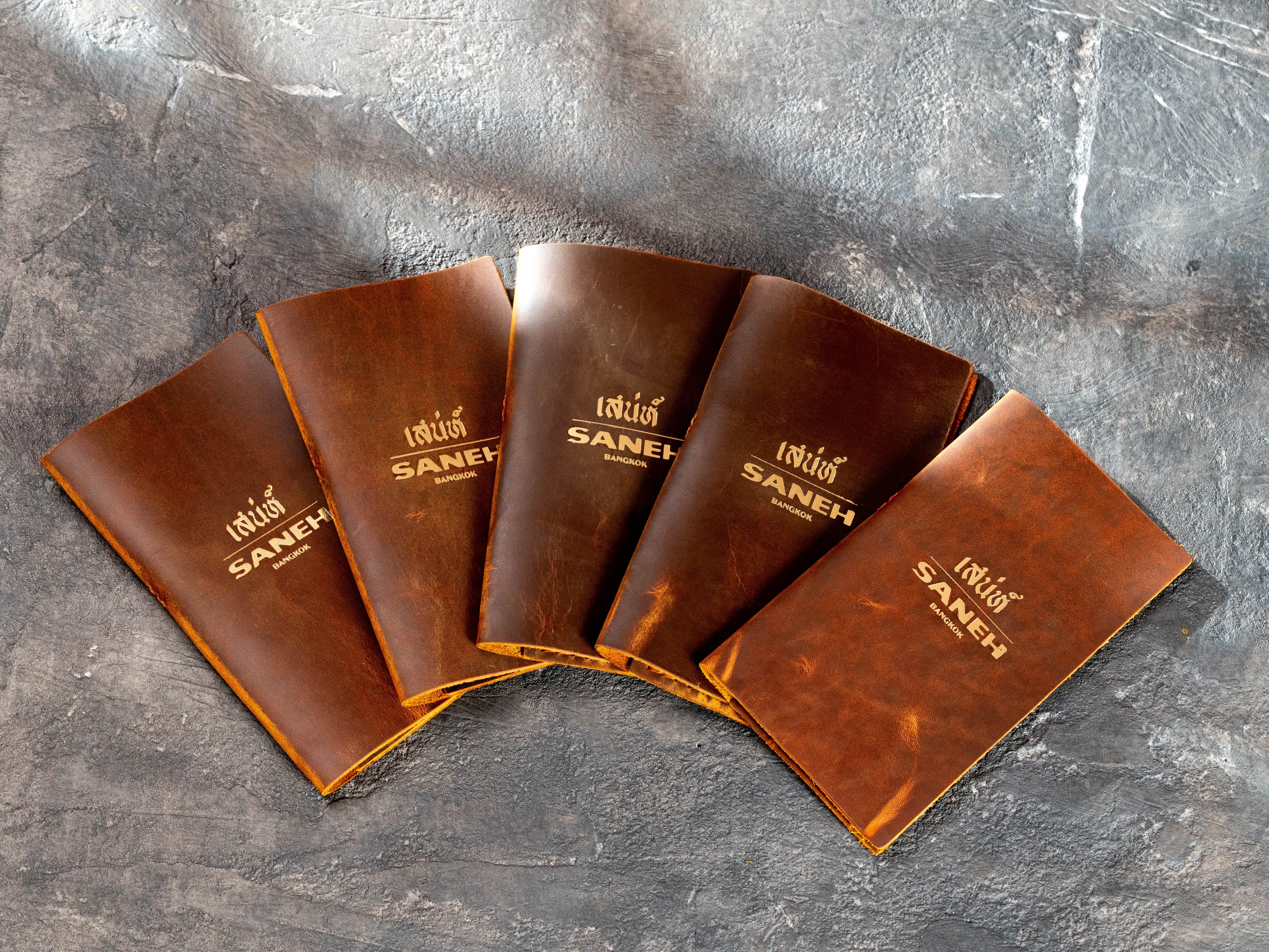 Custom chestnut leather check presenters with gold restaurant logo in a bulk hospitality order
