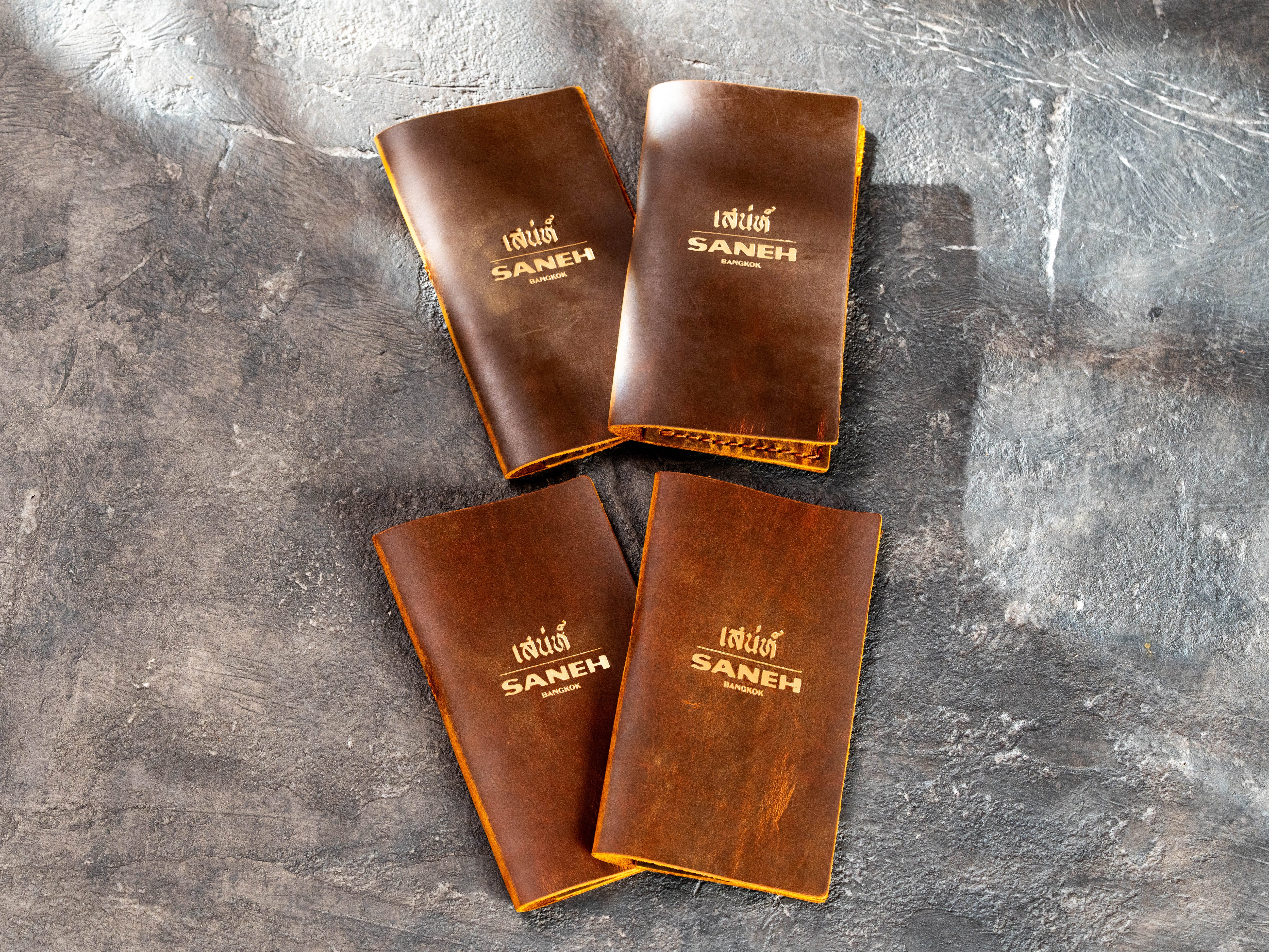 Four handmade chestnut leather restaurant bill holders with custom gold logo