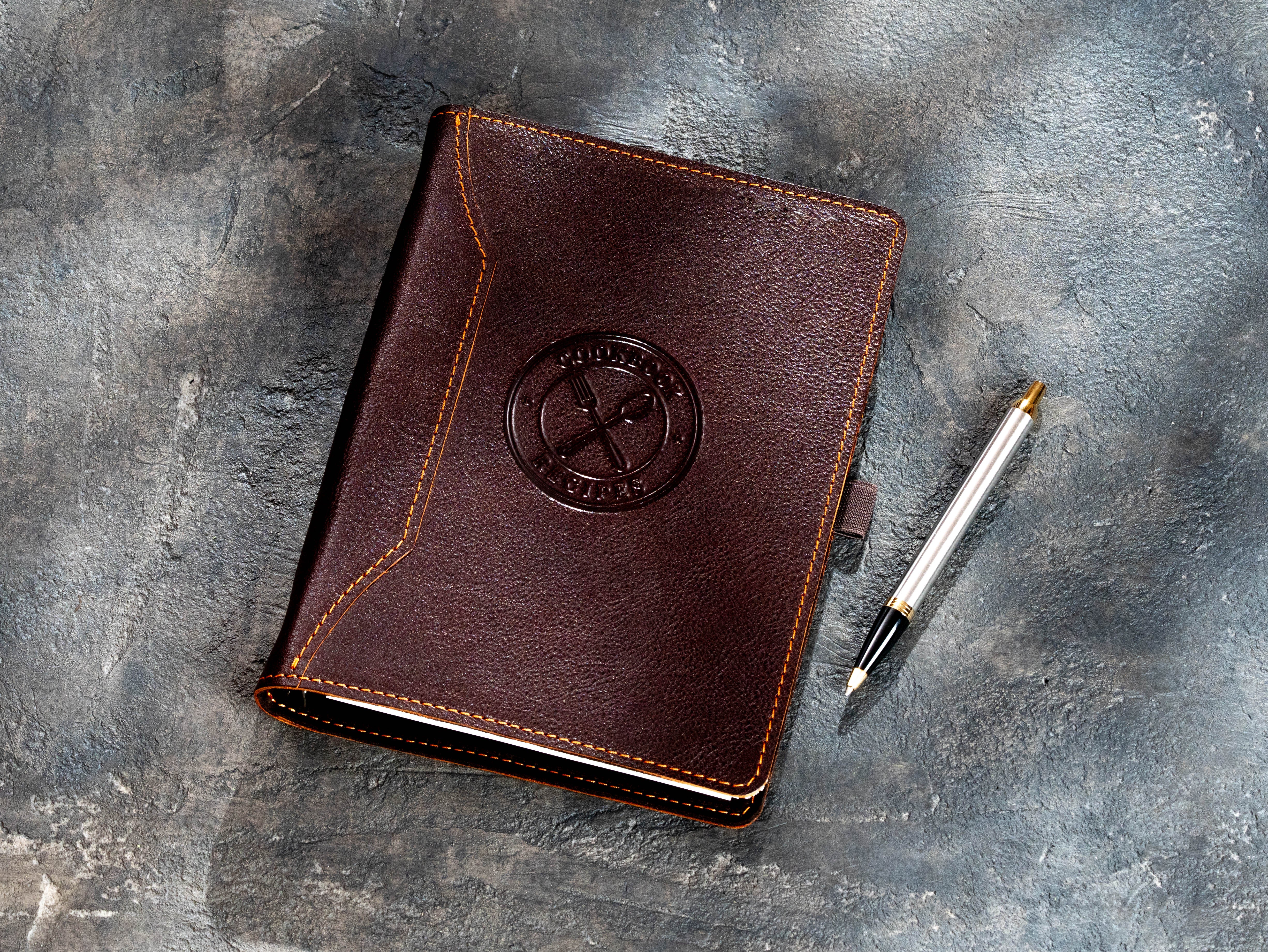 Dark brown leather recipe binder with Cookbook Recipes embossing and pen beside the cover