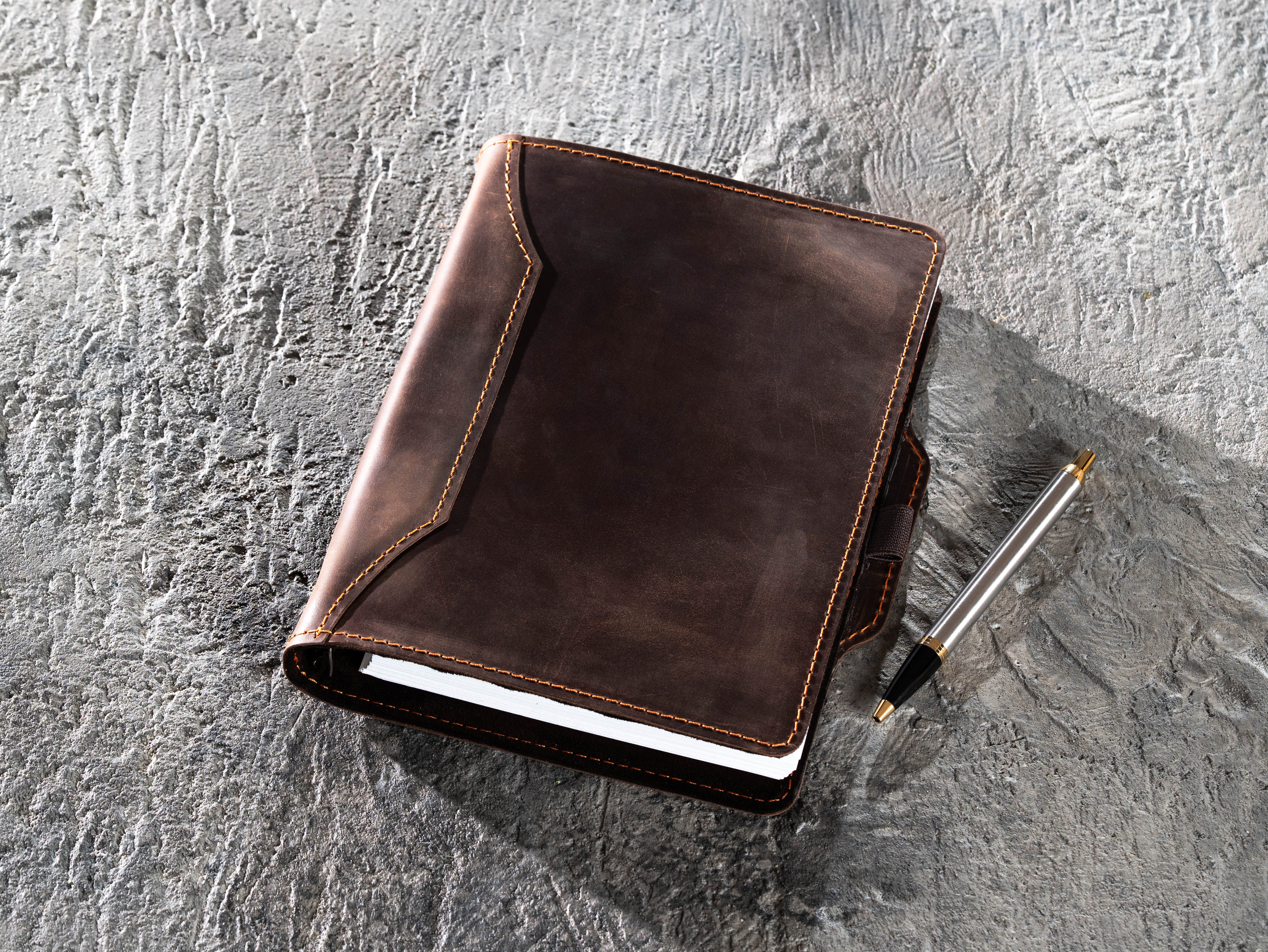 Dark brown leather A5 binder notebook shown with a pen beside the cover