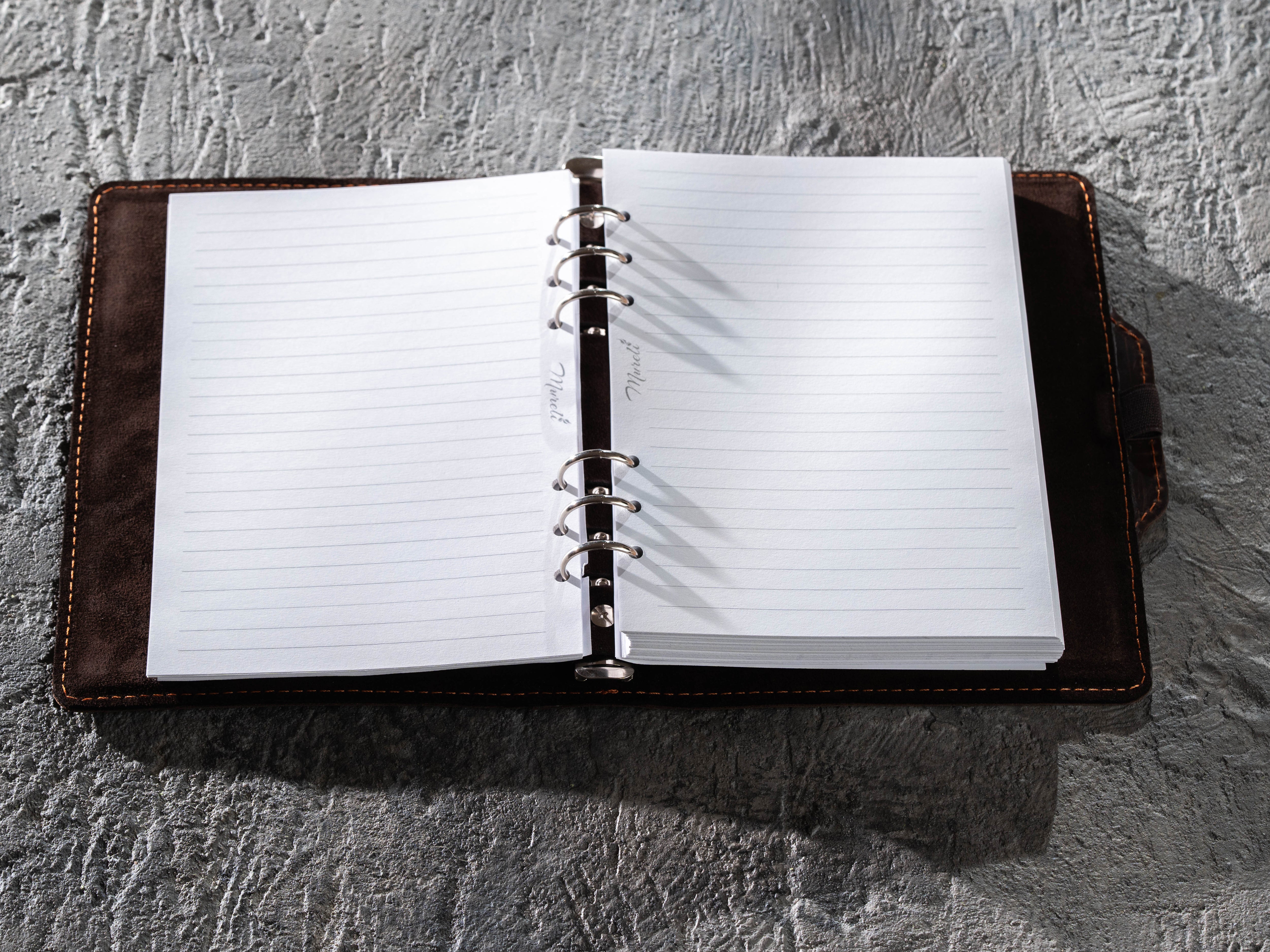 Dark brown leather A5 binder notebook open with lined paper attached to the six-ring mechanism