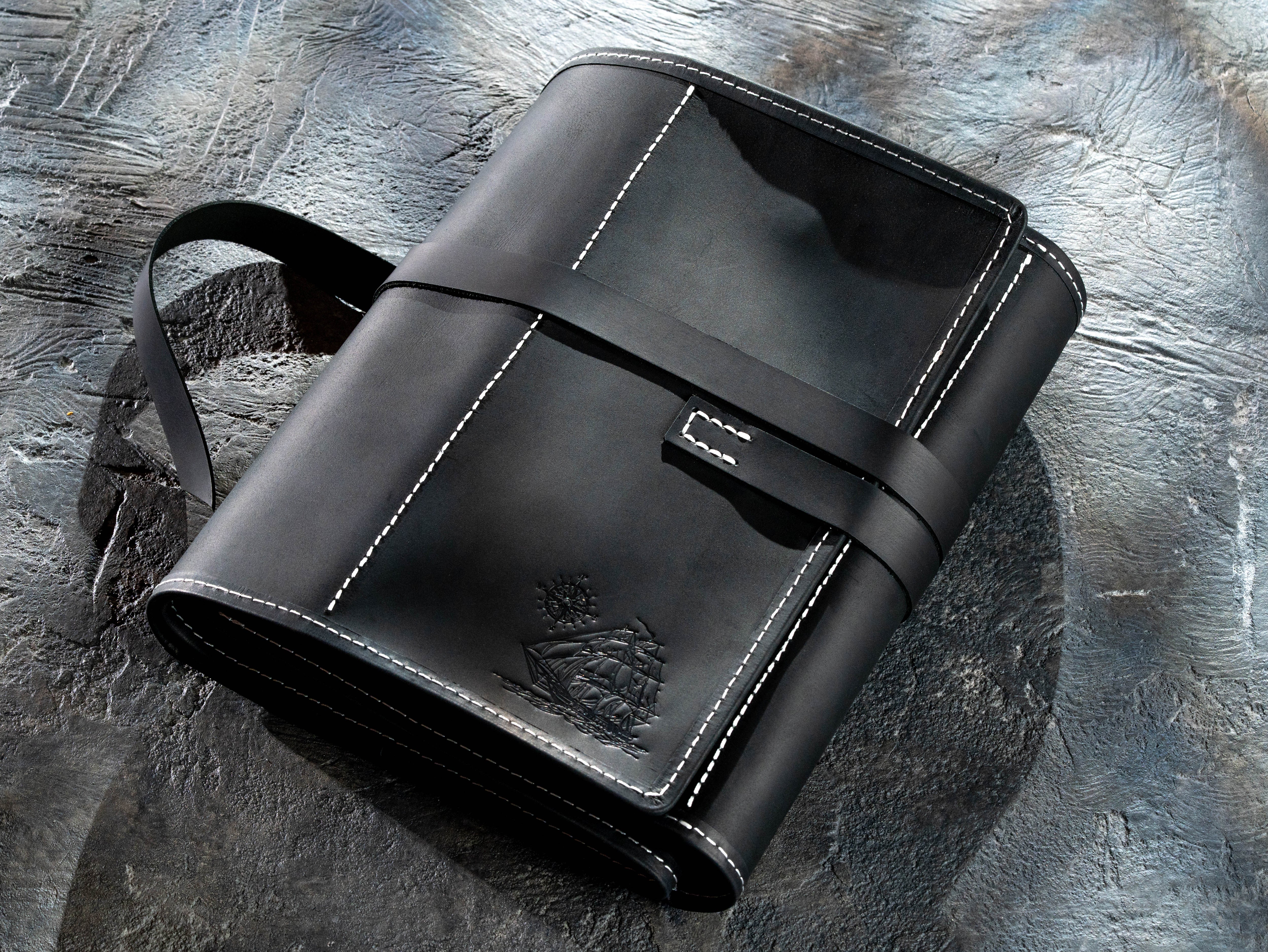 Closed black leather artist organizer with wraparound straps and embossed ship design