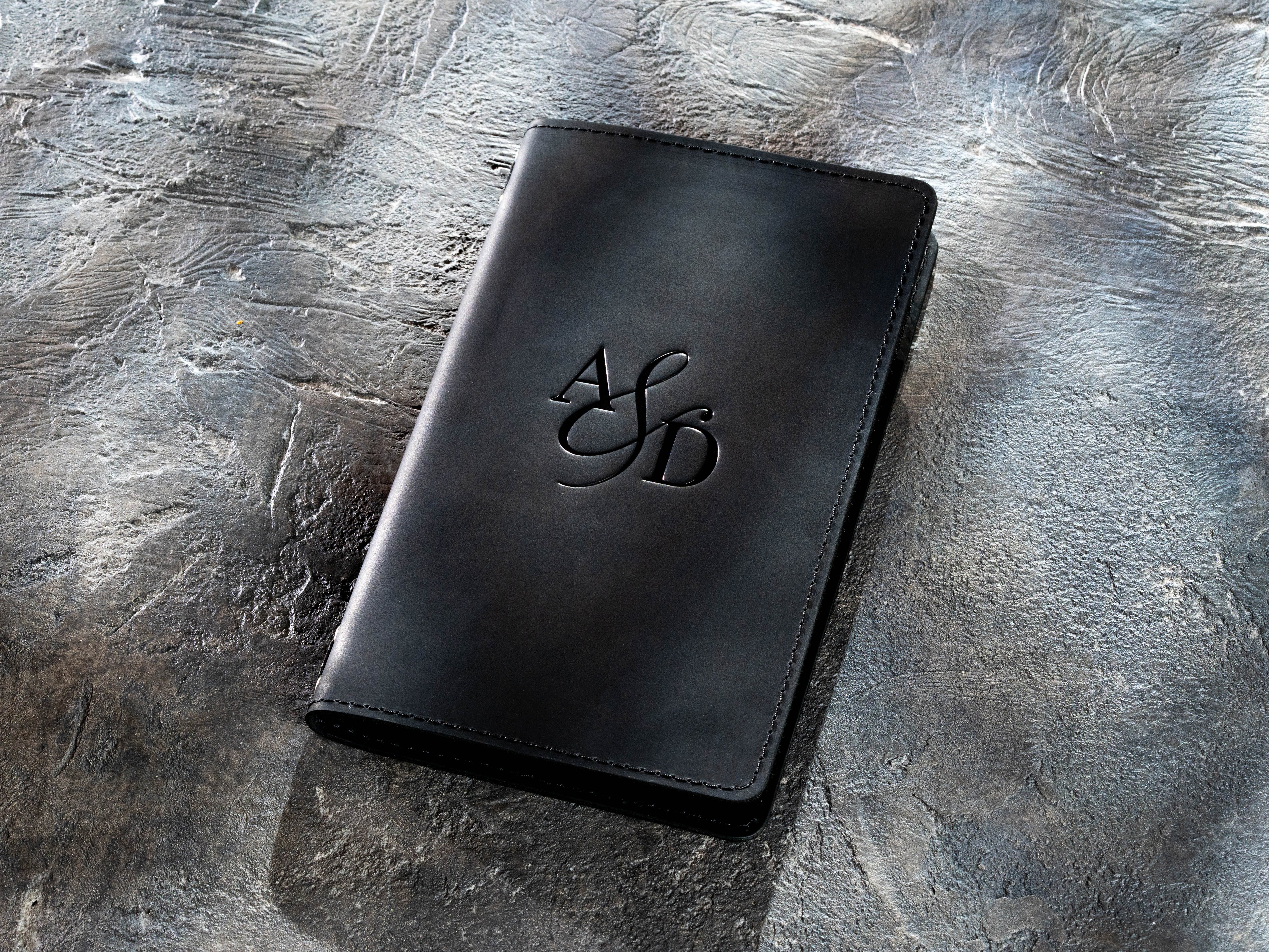 Closed black leather menu cover without personalization on a textured gray background