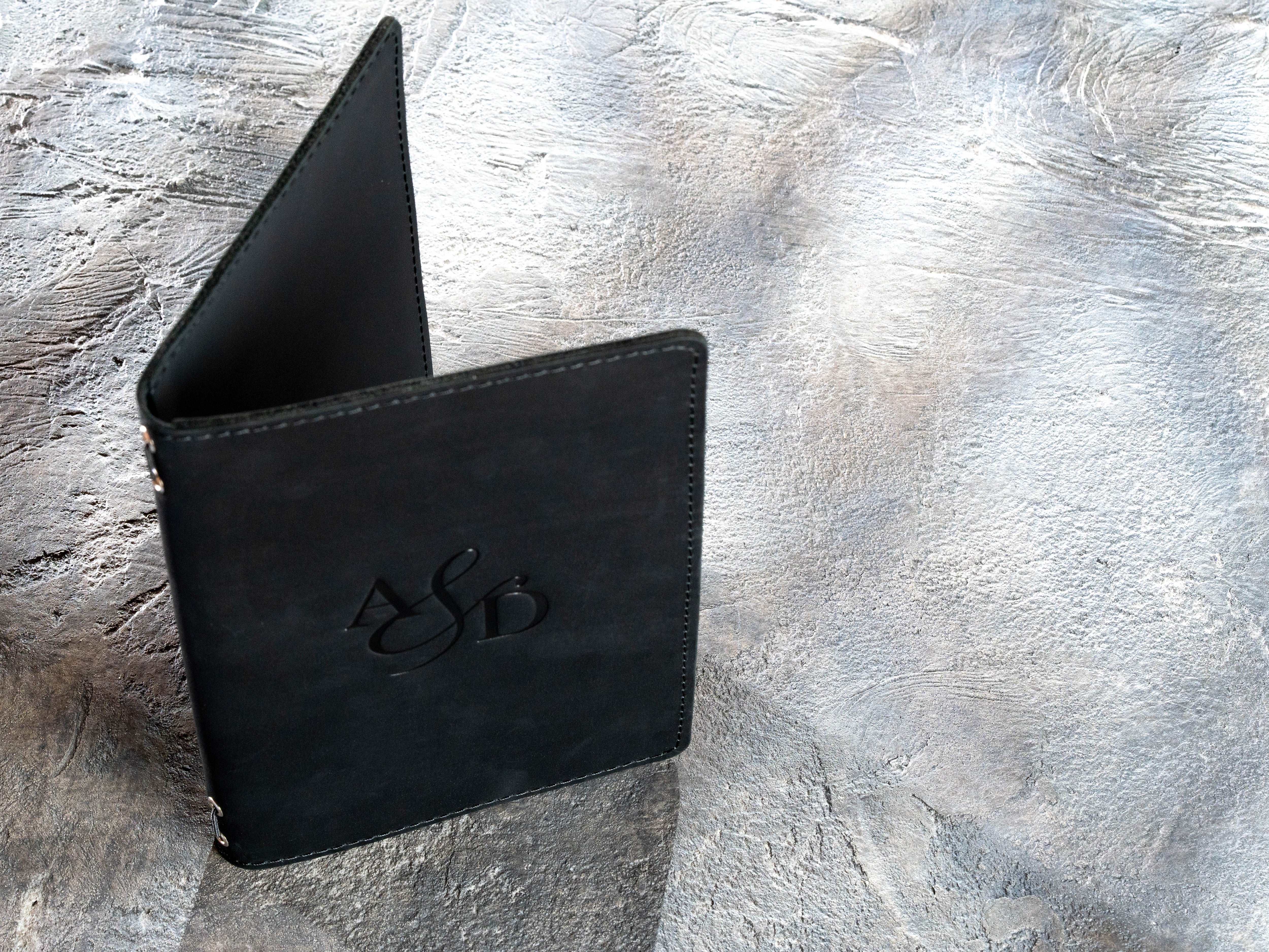 Standing black leather menu cover showing flexible spine and personalized front design