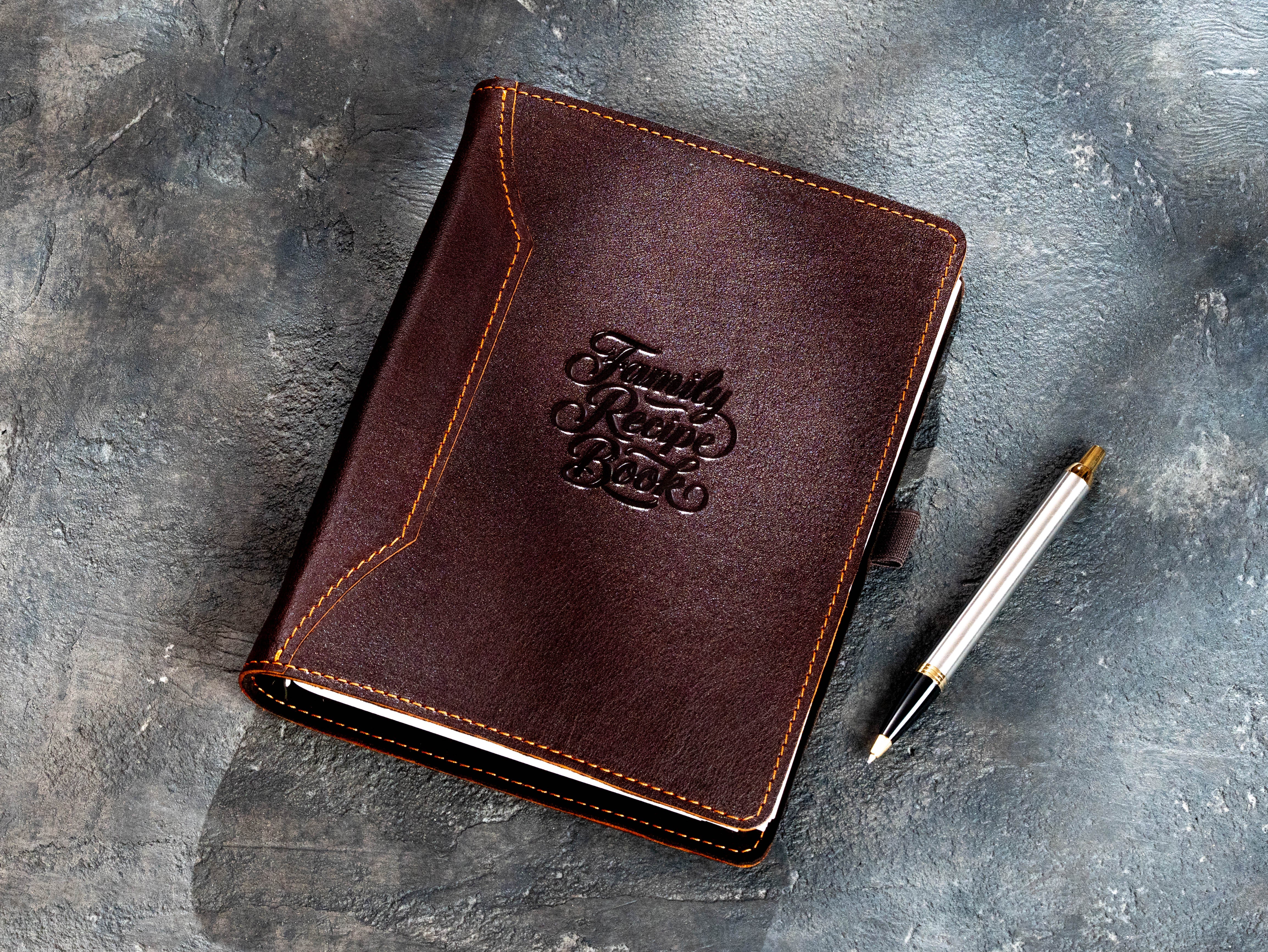 Dark brown leather recipe binder with Family Recipe Book embossing and pen beside the cover