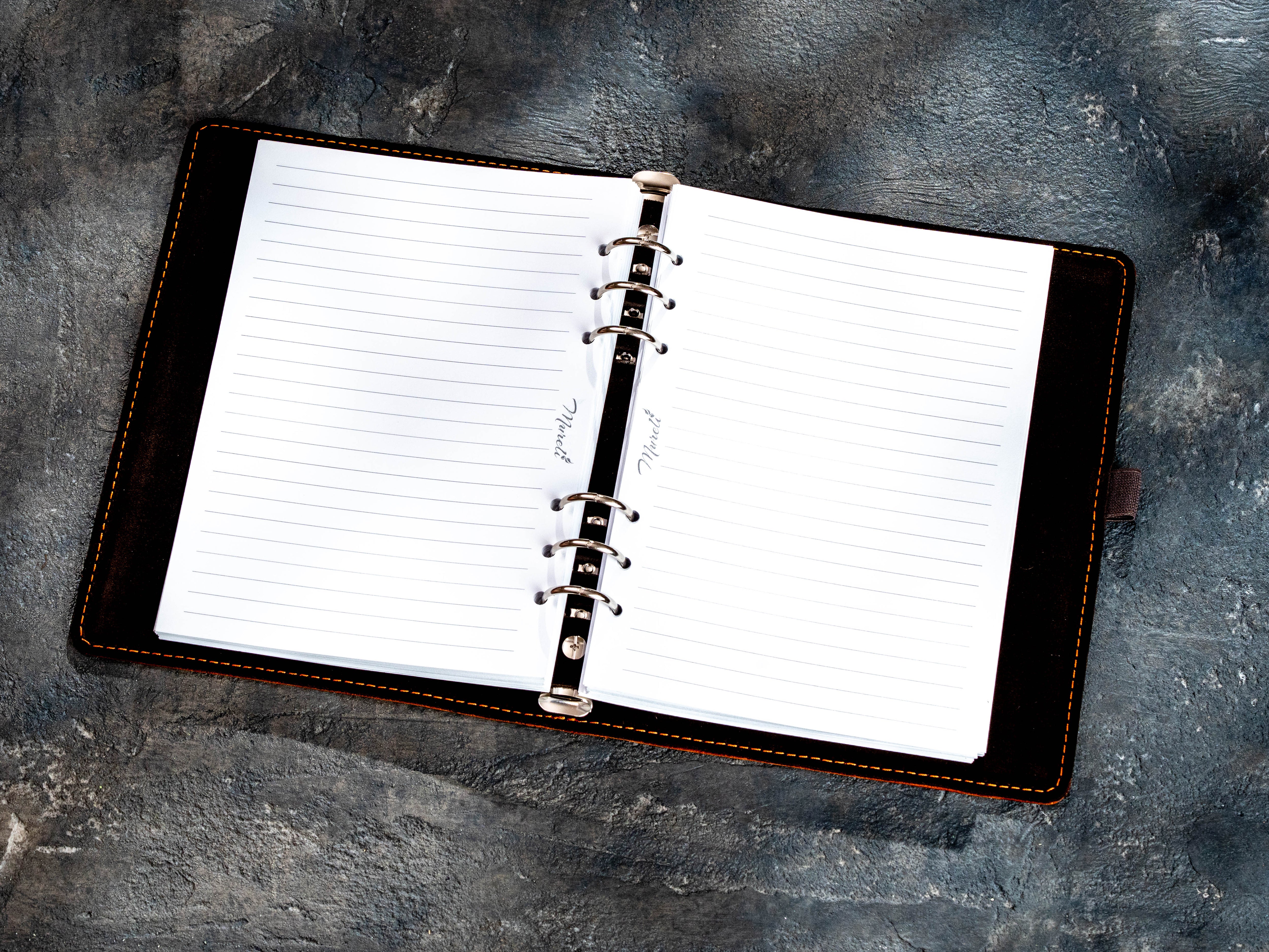 An open ring-bound planner or notebook with lined white pages and a black cover, photographed from above on a textured gray surface.