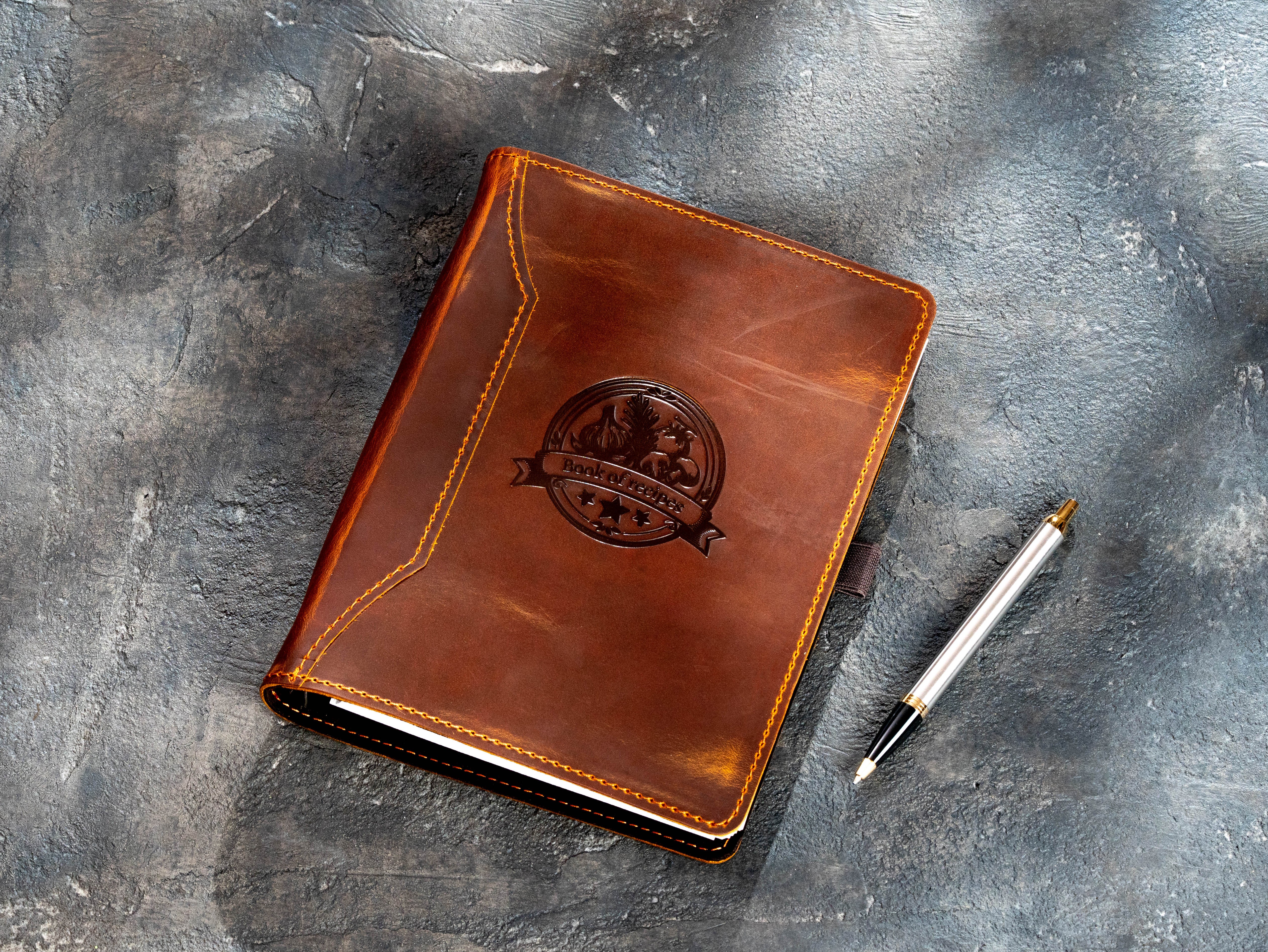 Chestnut leather recipe organizer with vintage food emblem and pen beside the cover
