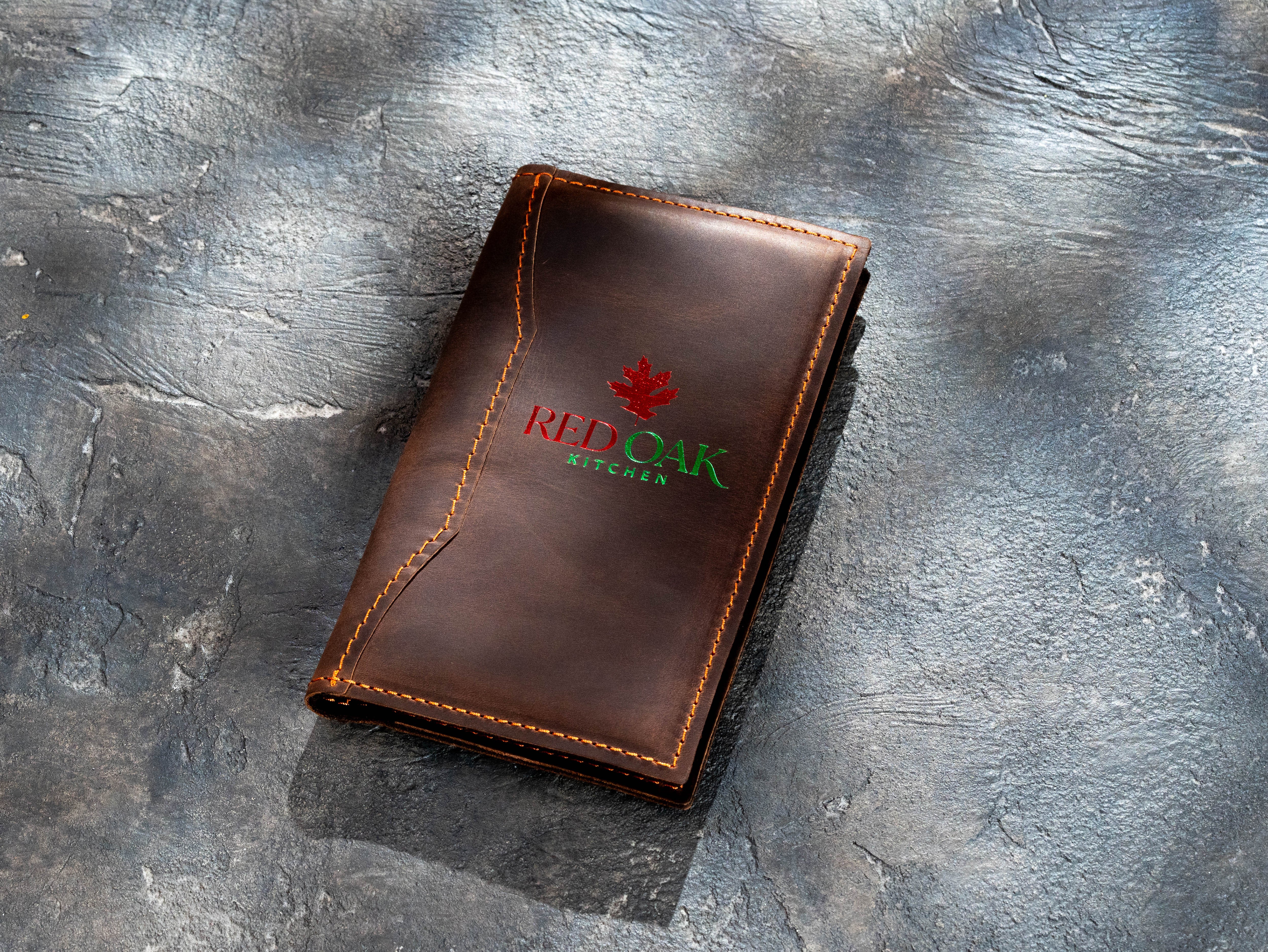Closed brown leather restaurant check presenter with custom red and green foil branding
