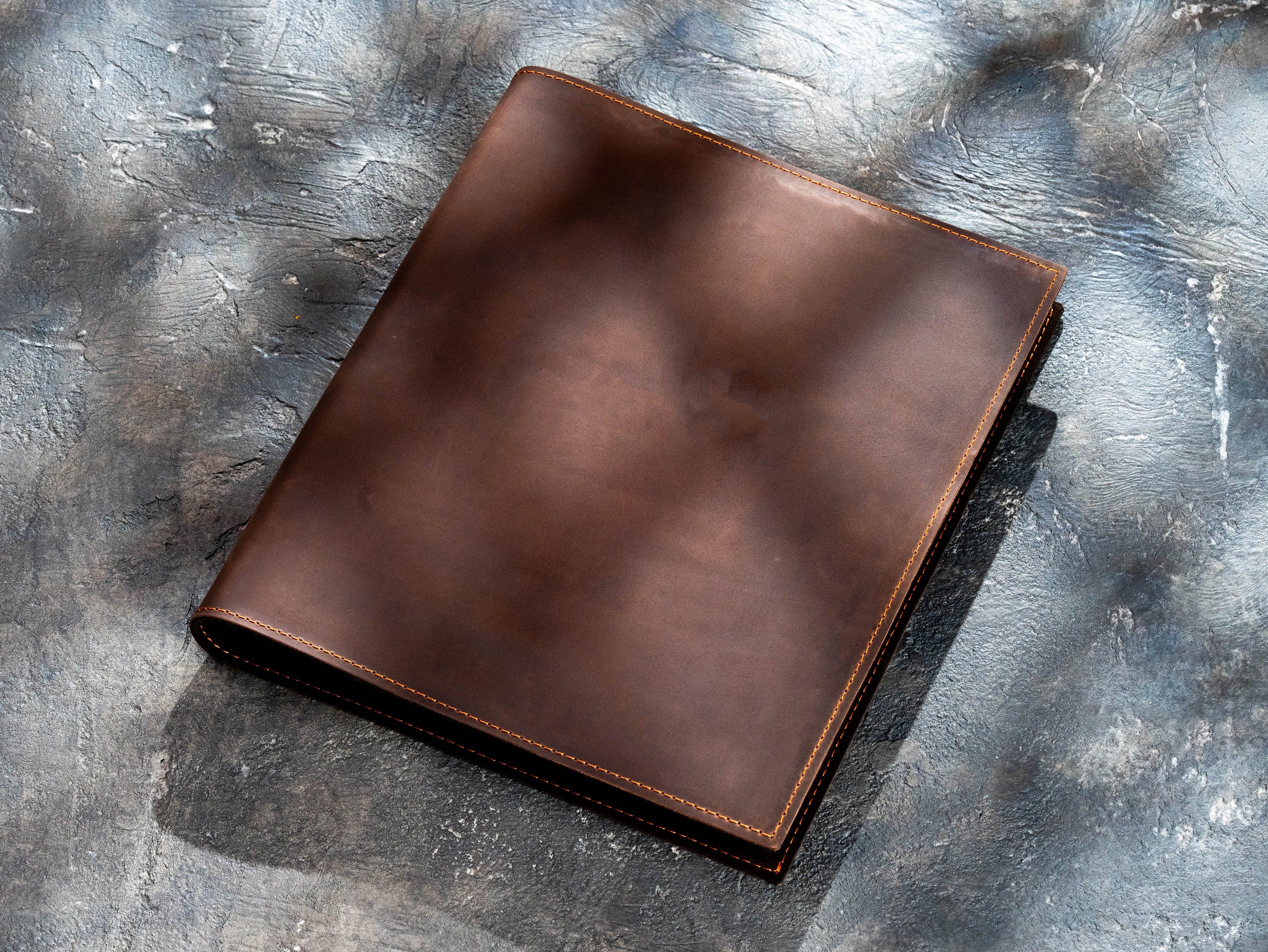 Closed brown leather 3-ring binder shown without branding on a textured gray background