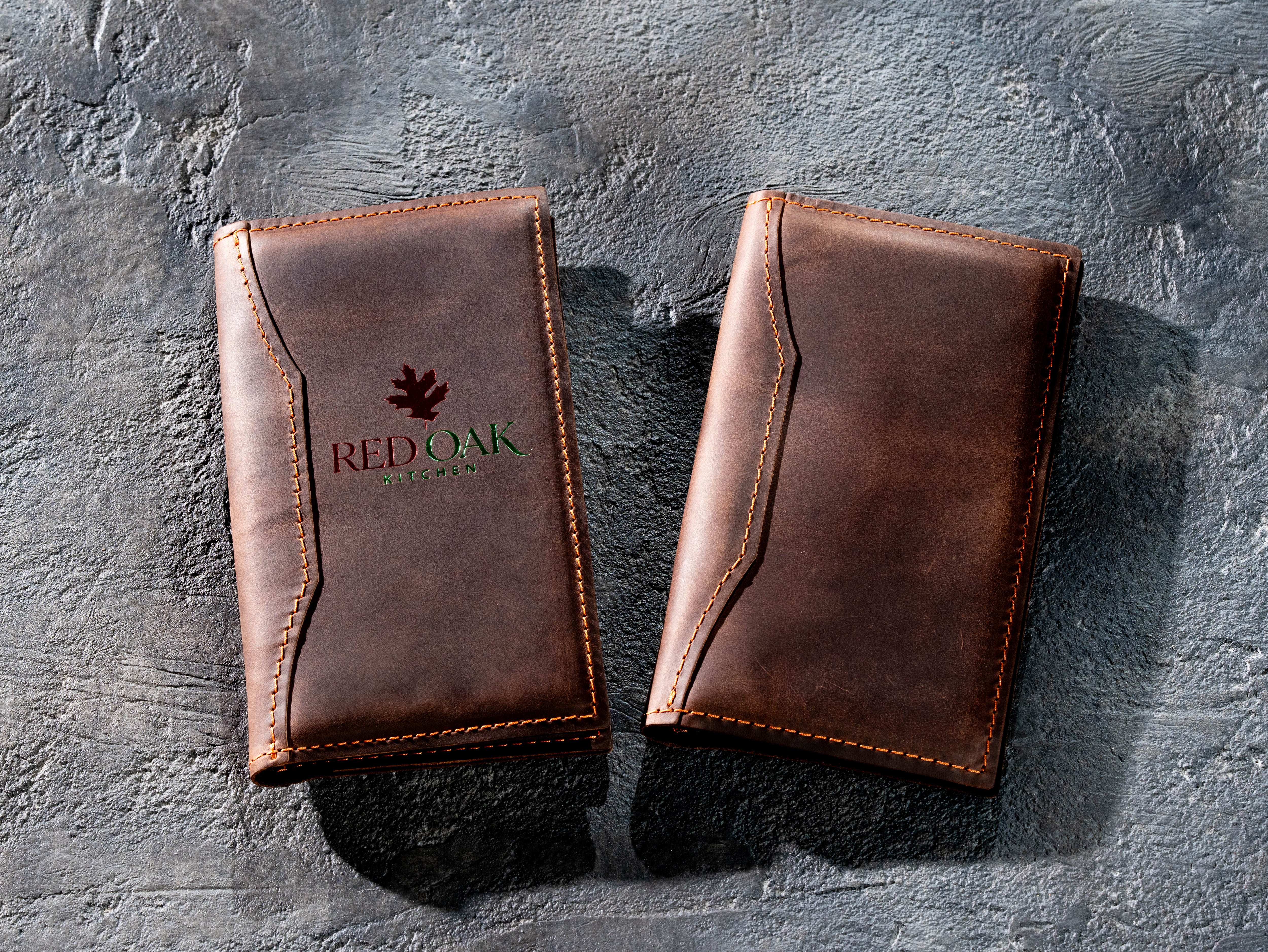 Pair of brown leather restaurant bill holders with custom logo and stitched edges