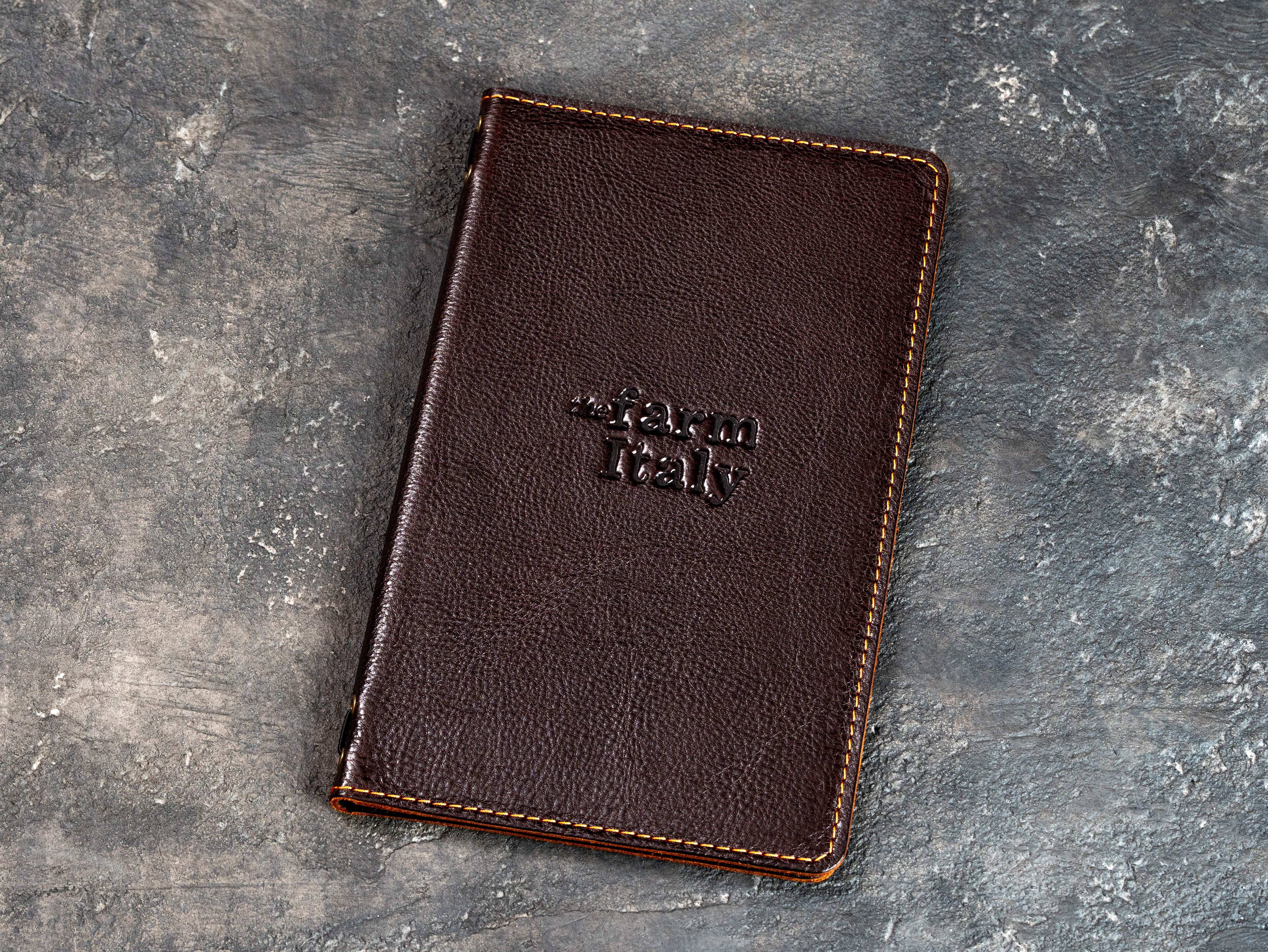 Closed cognac leather restaurant menu cover with a custom embossed logo on the front