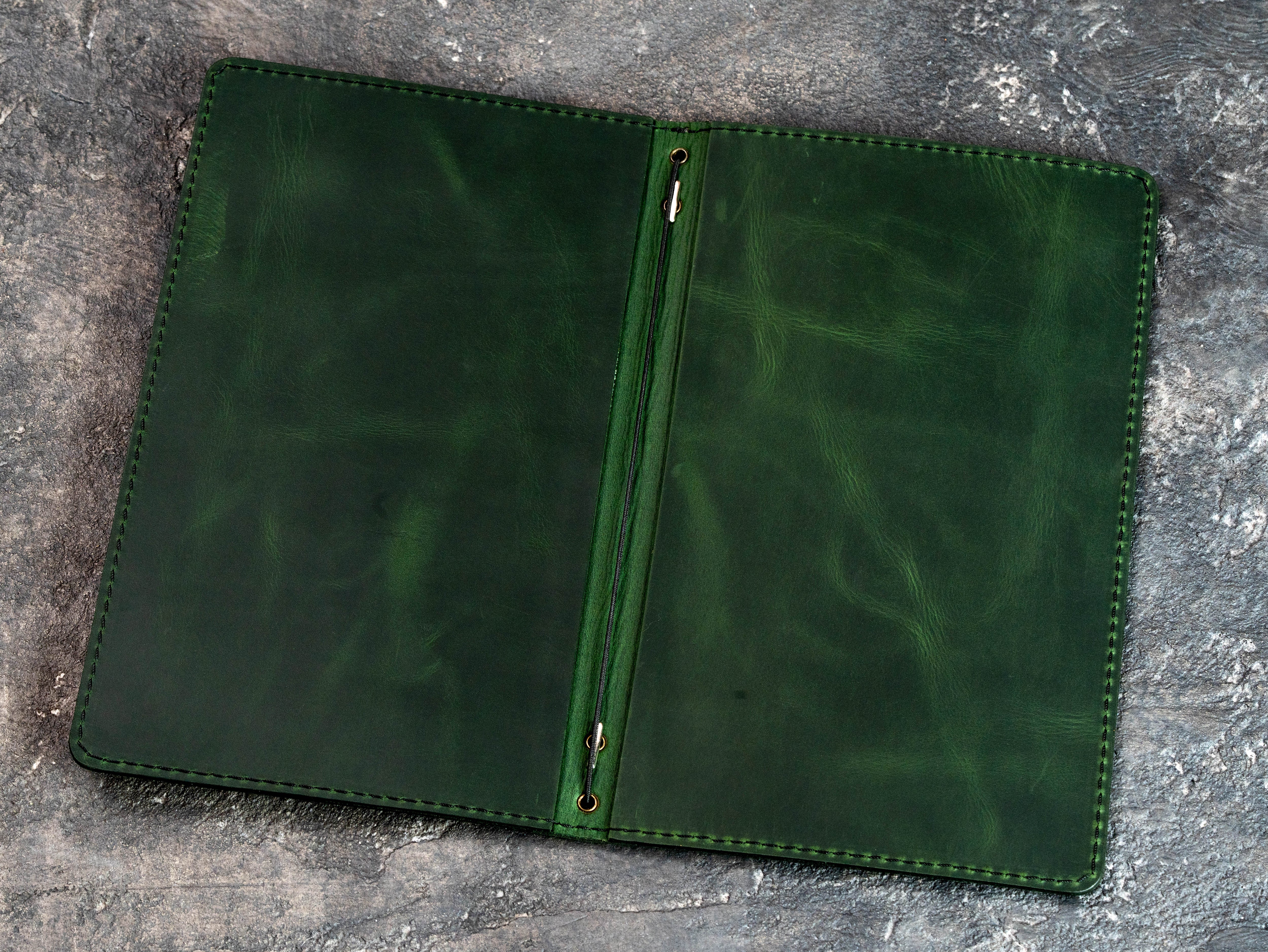 Green leather menu cover shown open without pages, highlighting the central elastic binding