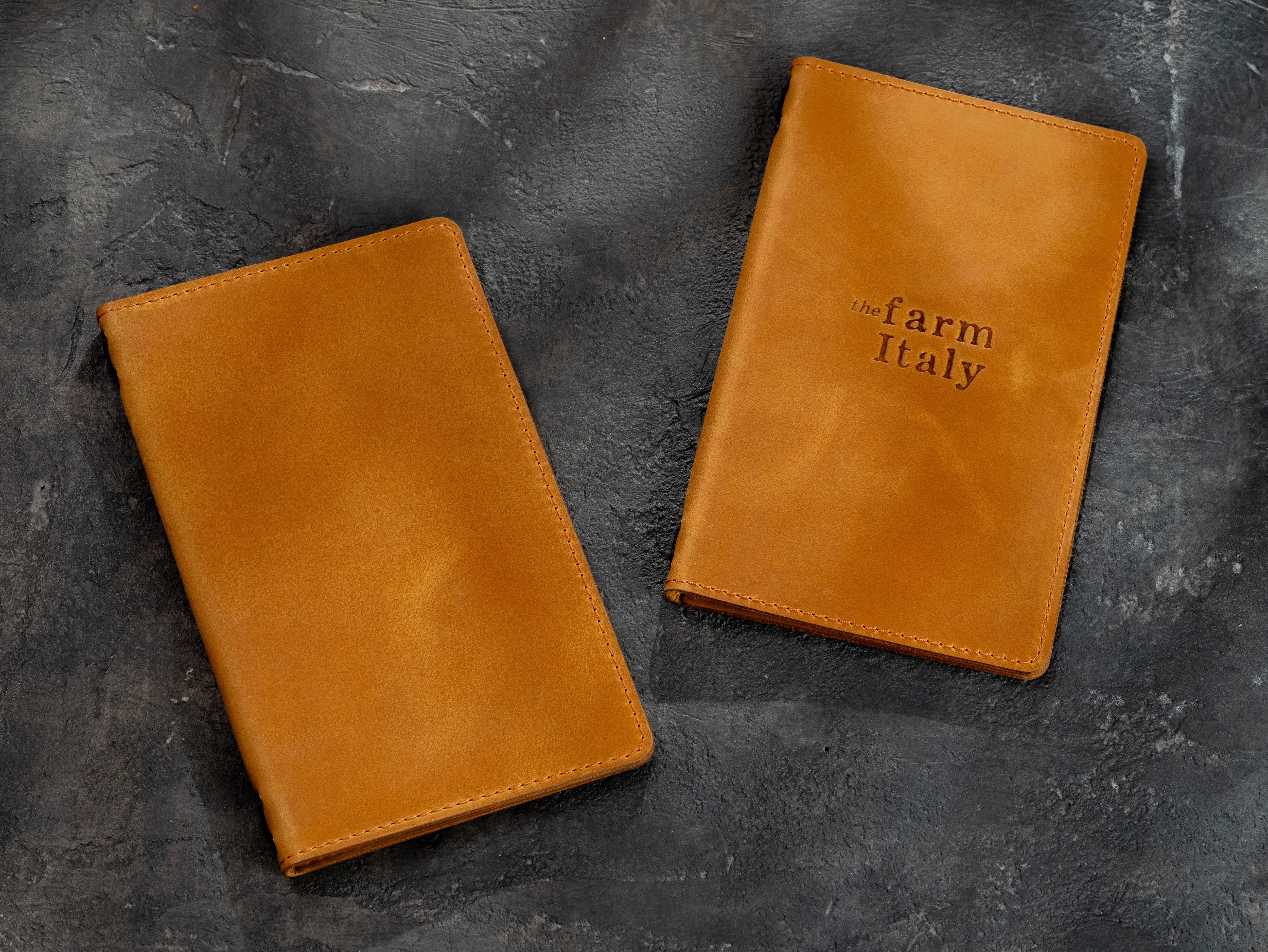 Two golden yellow leather restaurant menu covers shown closed, one with a custom embossed logo